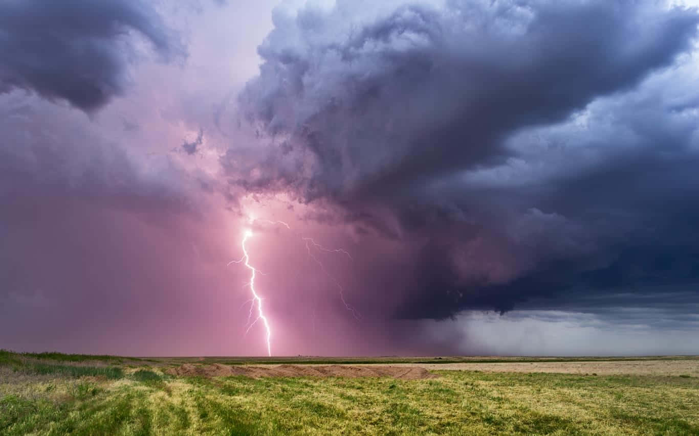 閃電 桌布 壁紙 — 一道強大的閃電在黃昏時分劃破廣闊田野上空戲劇性的紫色和灰色暴風雲。