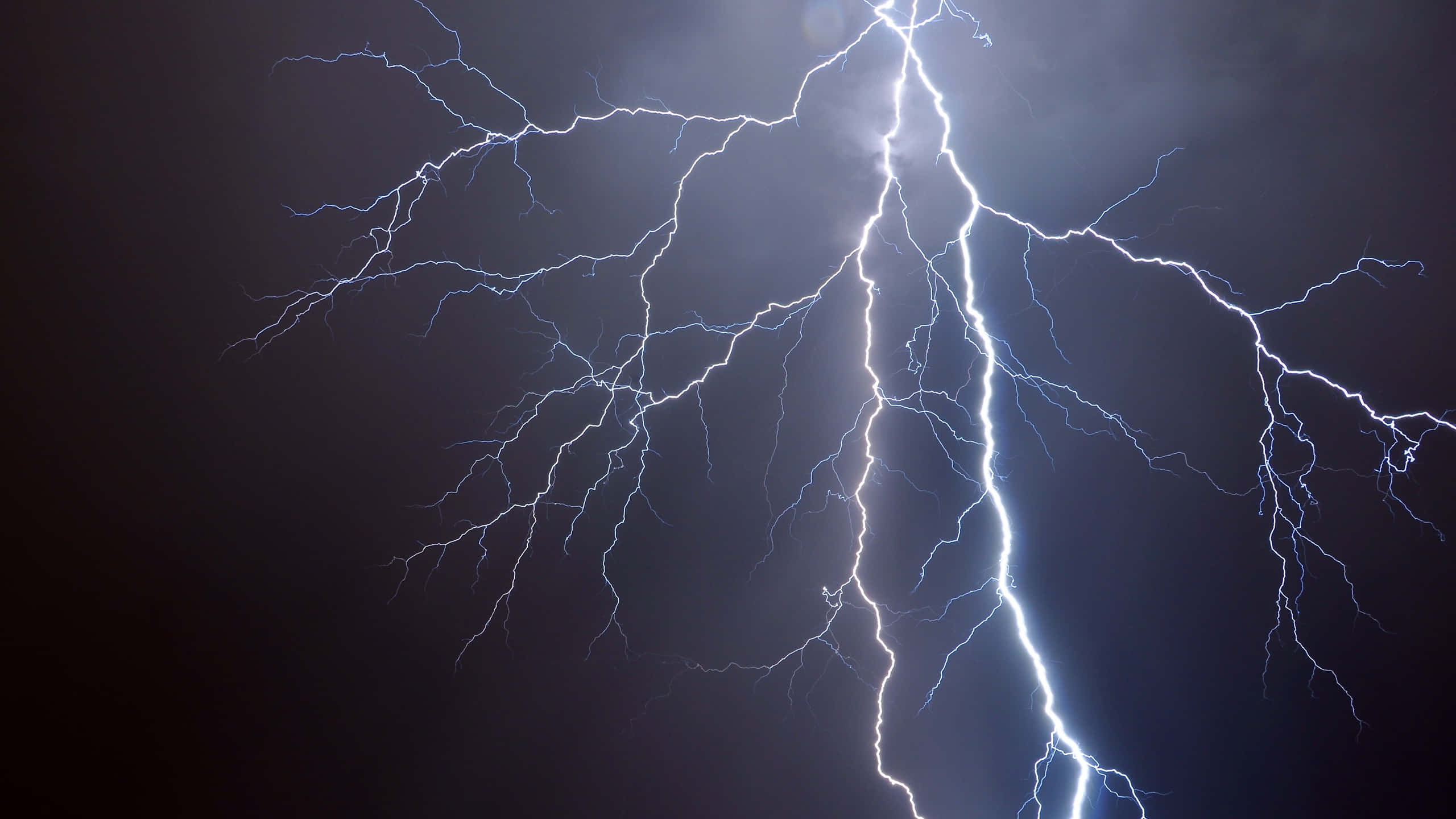閃電 桌布 壁紙 — 一道強大的閃電在黑暗的暴風雨天空中分叉出藍白色的枝條，照亮了雲層。