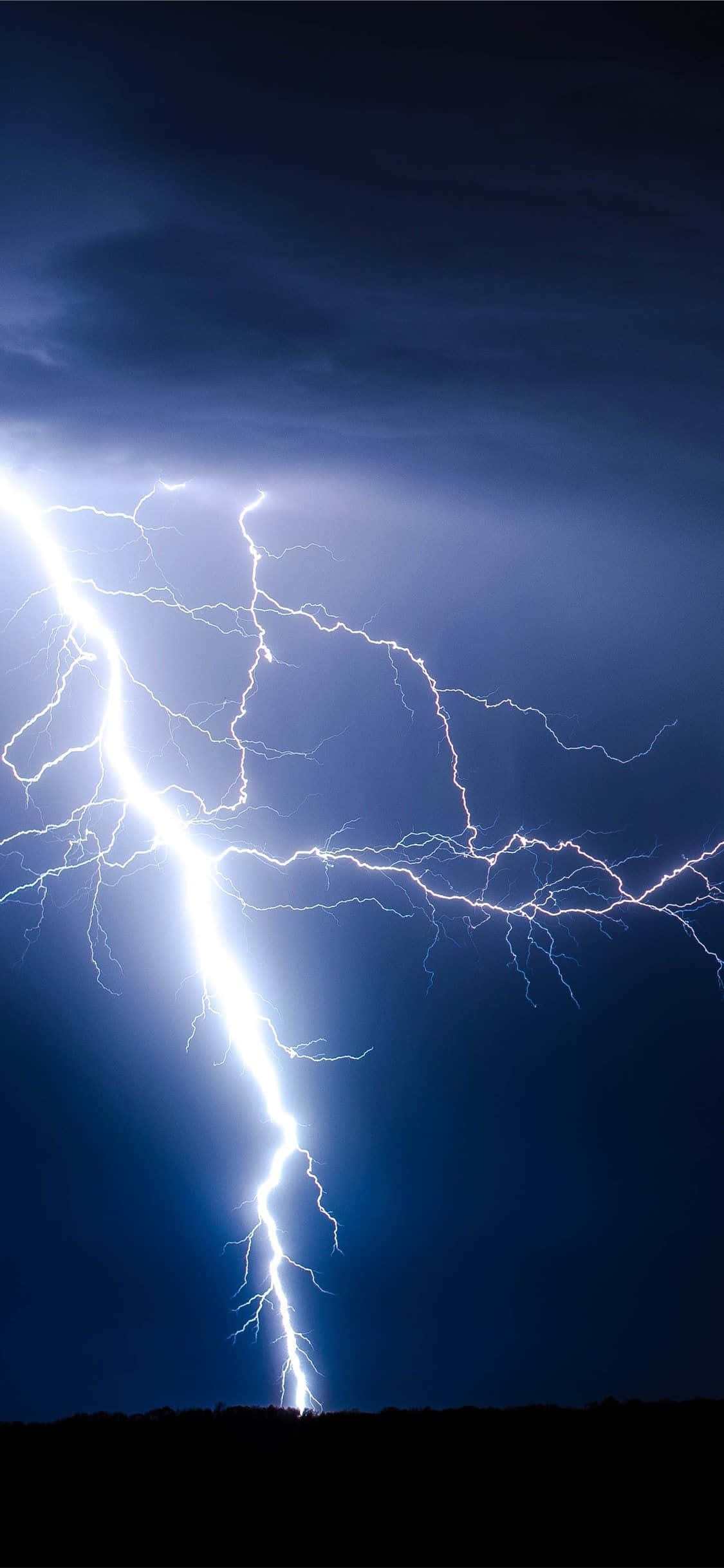 電力 桌布 壁紙 — 一道強大的閃電在黑暗的暴風雨天空中分叉，照亮了下方遠處山丘的輪廓。