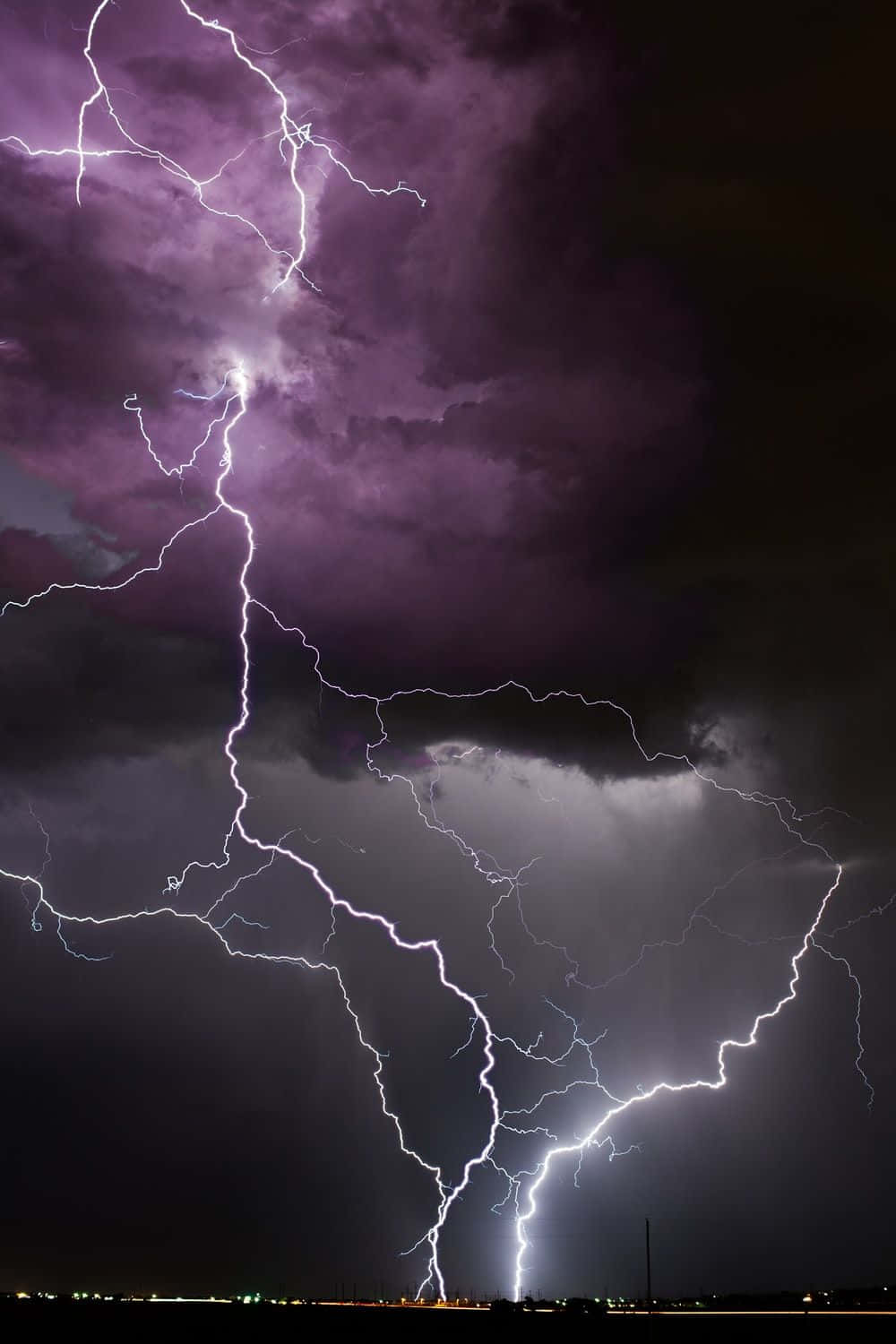 Thunderstorm 桌布 壁紙 — 一道強烈的紫色閃電劃破戲劇性的夜空，照亮遠方地平線上的黑暗暴風雲。