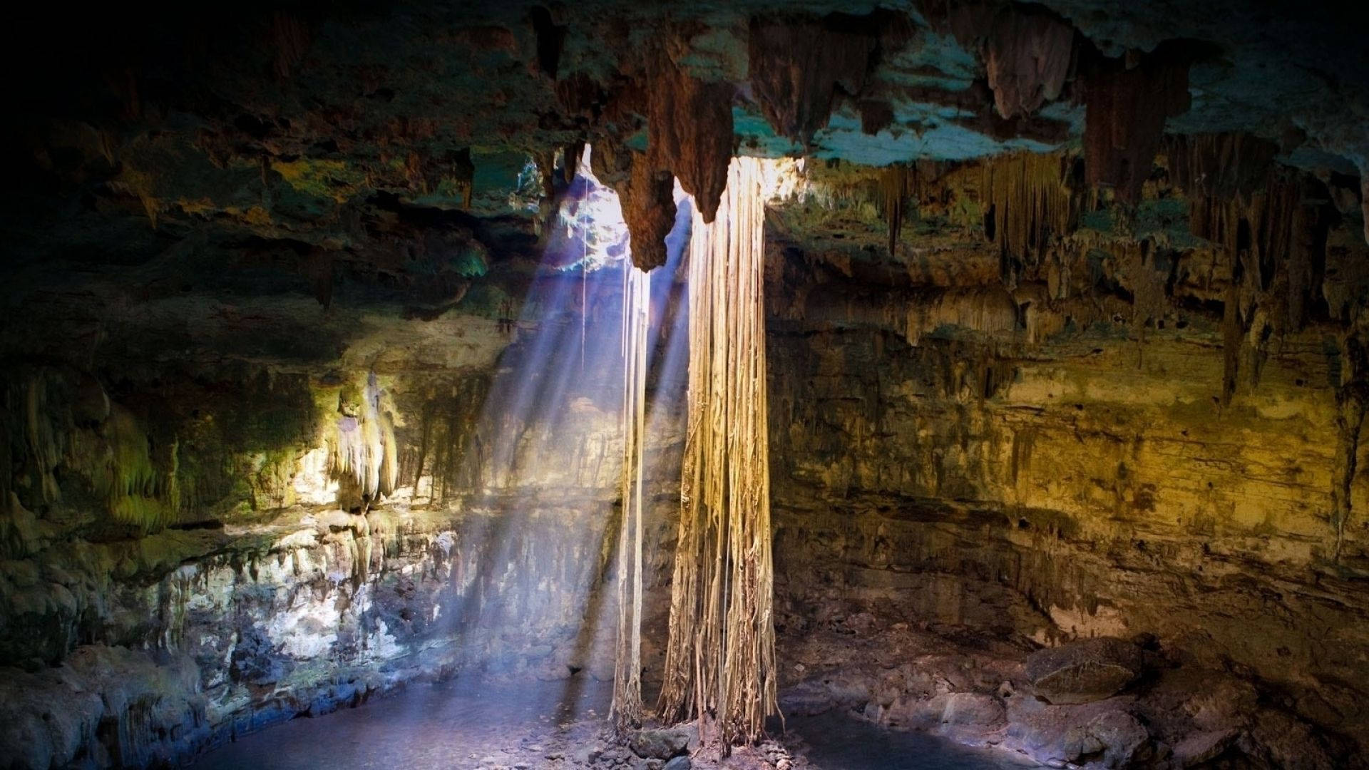 Cave 桌布 壁紙 — 一道戲劇性的光束穿過洞穴天花板，照亮了鐘乳石和崎嶇的岩壁，呈現大地色調。