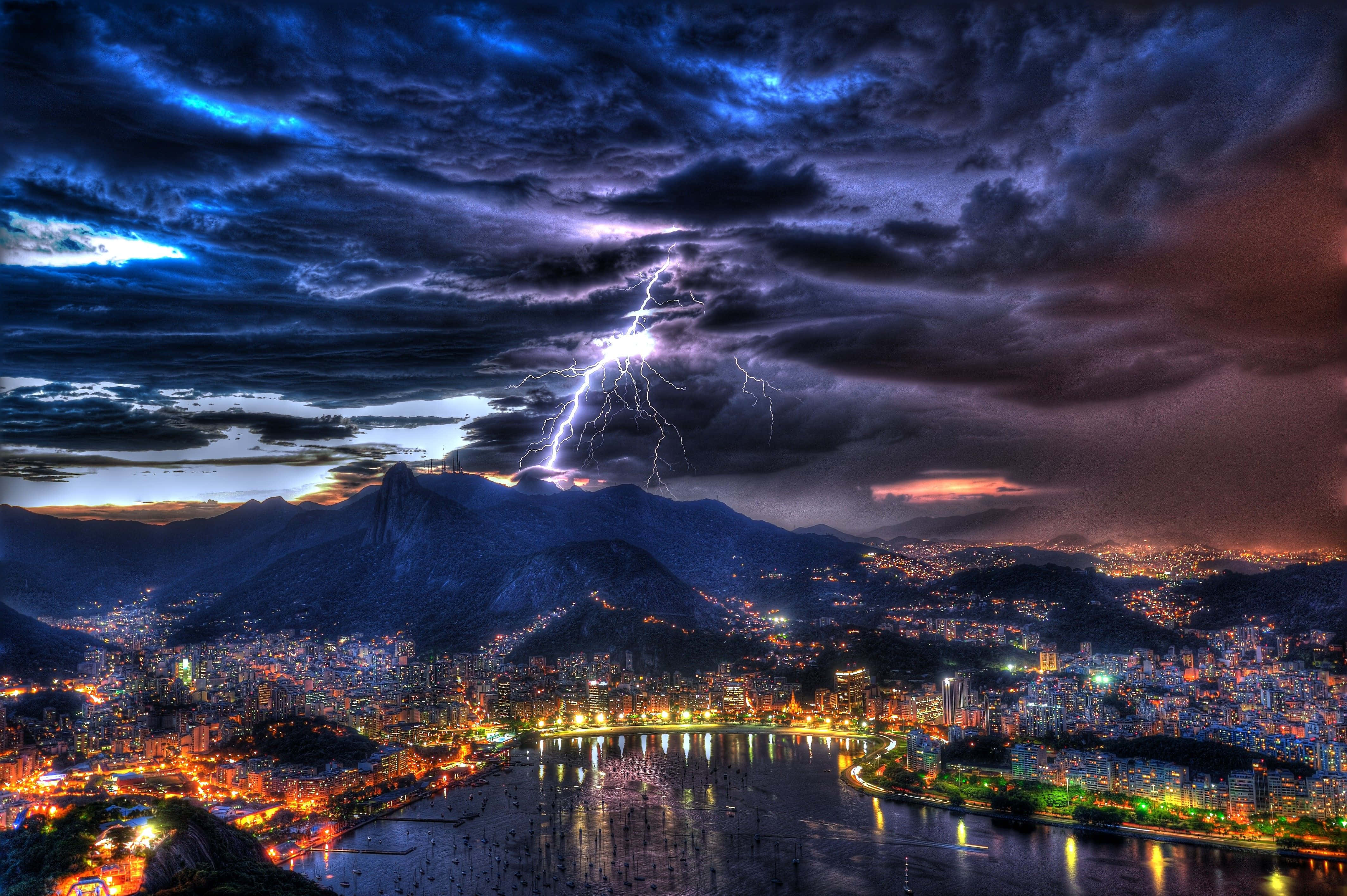 thunder 桌布 壁紙 — 一道戲劇性的閃電劃過黃昏時分坐落於山脈與閃耀海濱之間的廣闊城市。