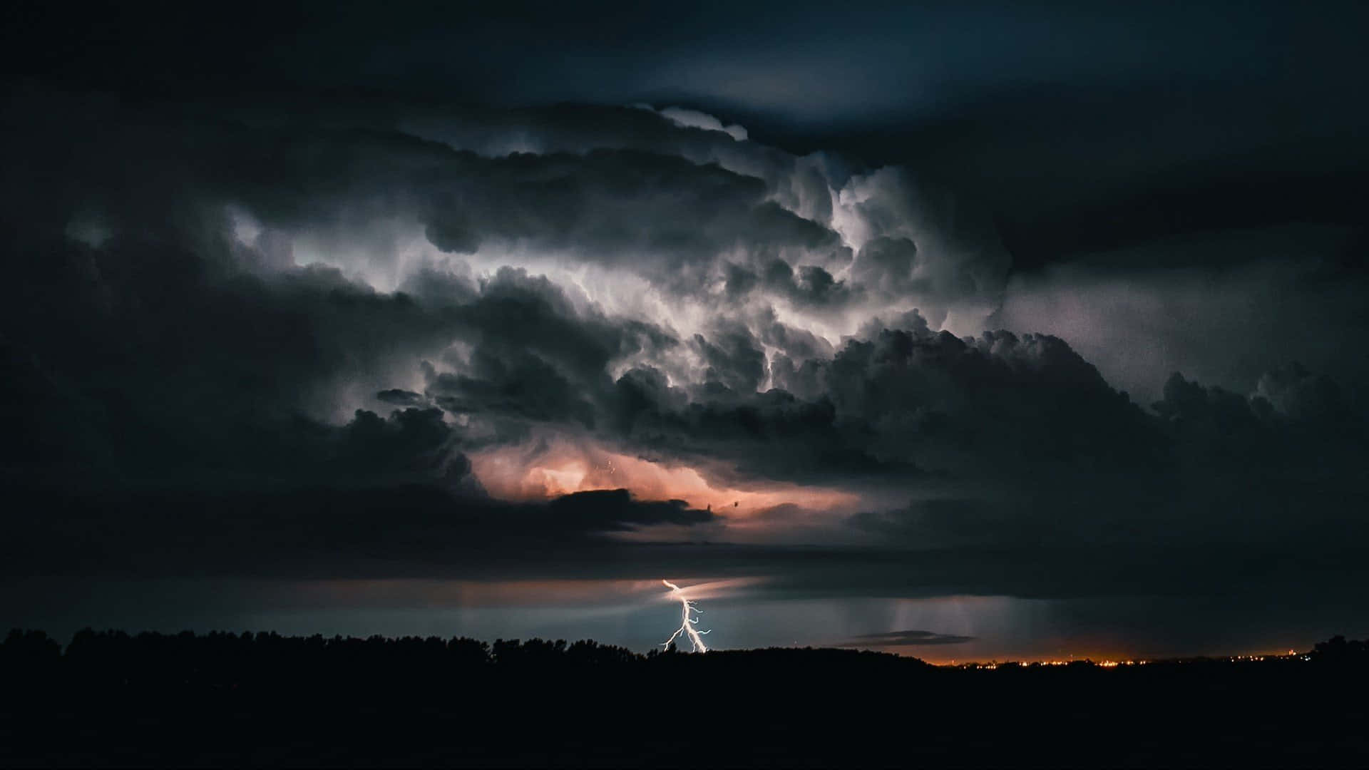 Thunderstorm 桌布 壁紙 — 一道戲劇性的閃電劈開高聳的暴風雲，籠罩著夜晚黑暗的森林輪廓。