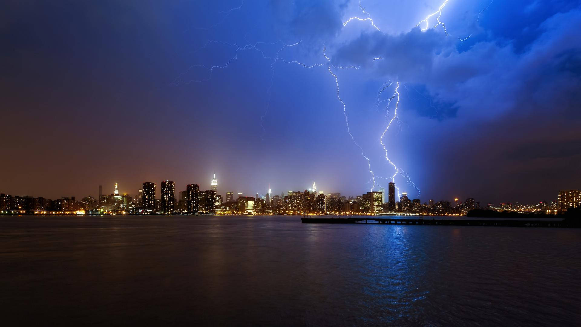 暴風 桌布 壁紙 — 一道戲劇性的閃電照亮了暴風雨之夜，城市天際線在黑暗的水面上閃爍倒映。
