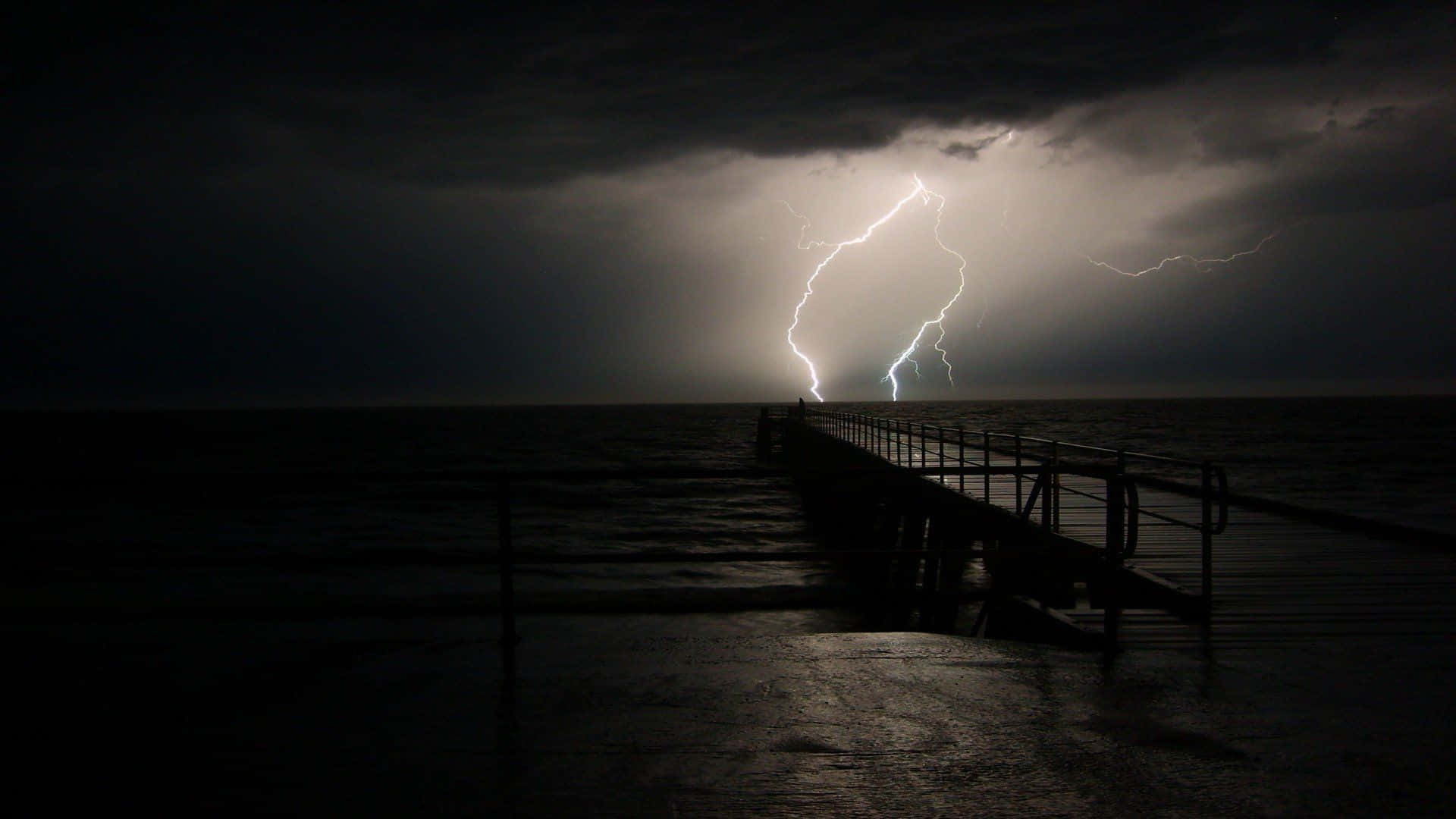 thunder 桌布 壁紙 — 一道戲劇性的閃電照亮了暴風雨夜空中延伸入海的黑暗碼頭。