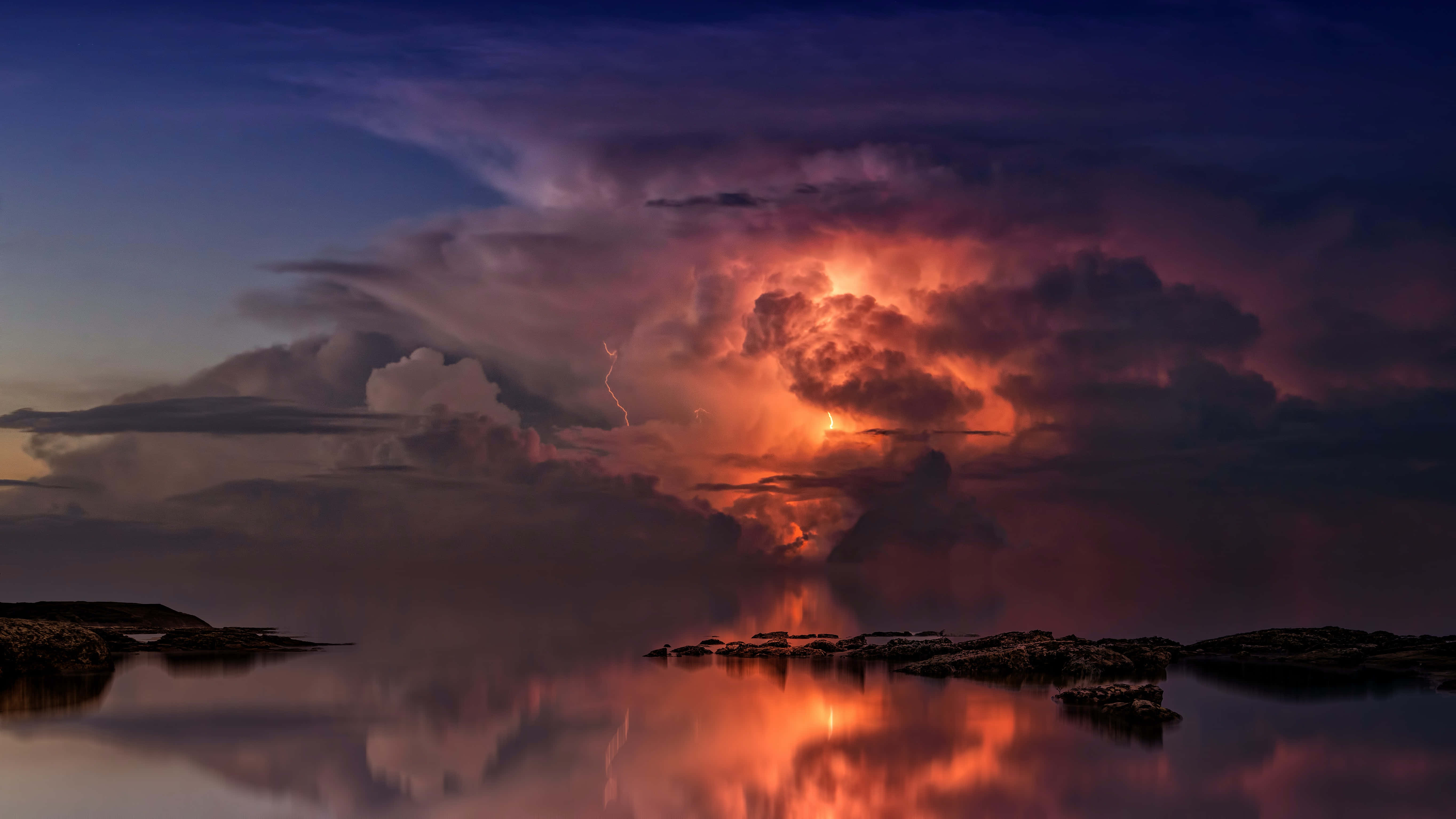 Clouds Aesthetics 桌布 壁紙 — 一道戲劇性的閃電照亮了暴風雲，平靜的水面反射出火熱的橙色和深紫色調。