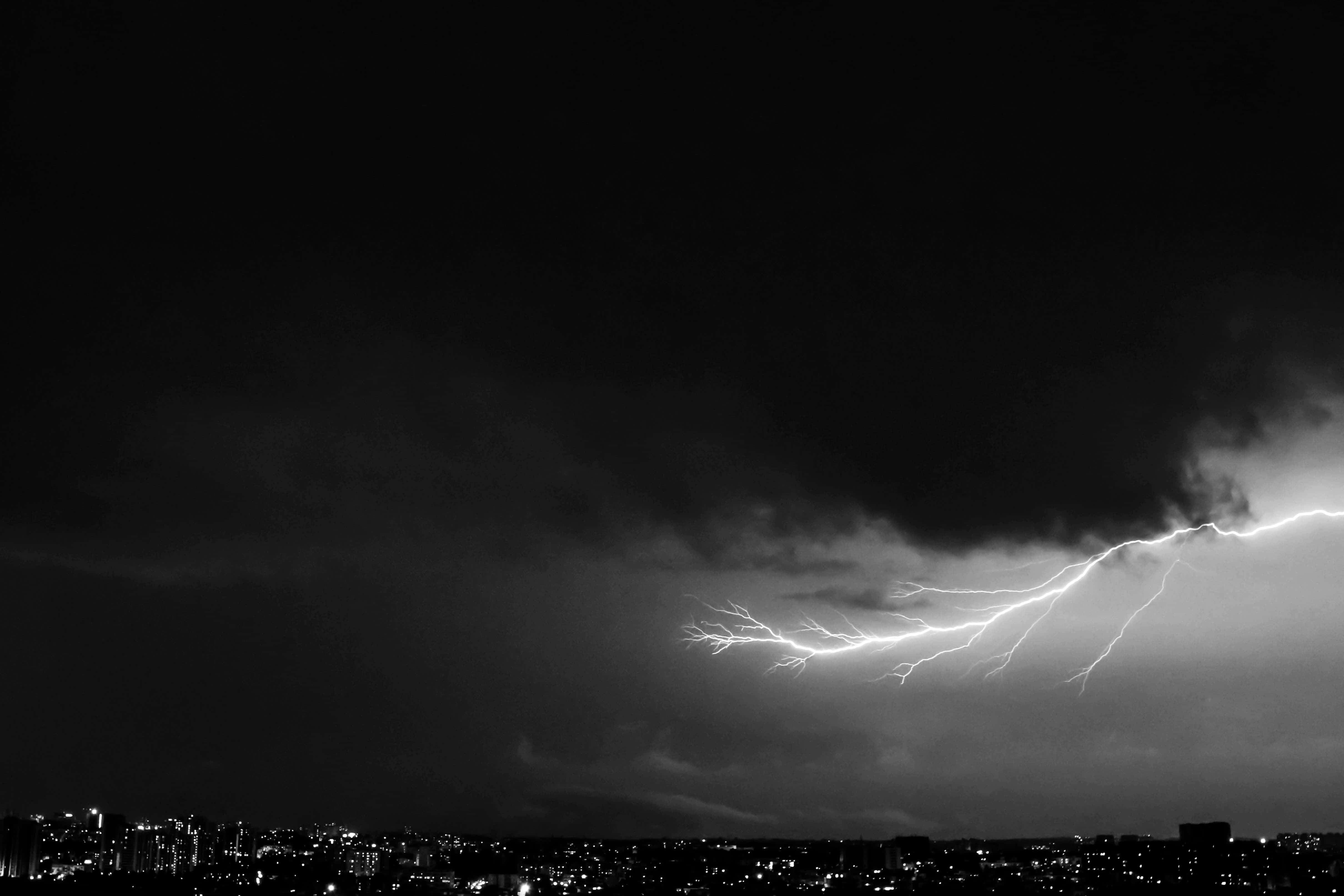 Dark Storm 桌布 壁紙 — 一道戲劇性的黑白閃電照亮了城市景觀上空的暴風雨夜空，伴隨著閃爍的燈光。