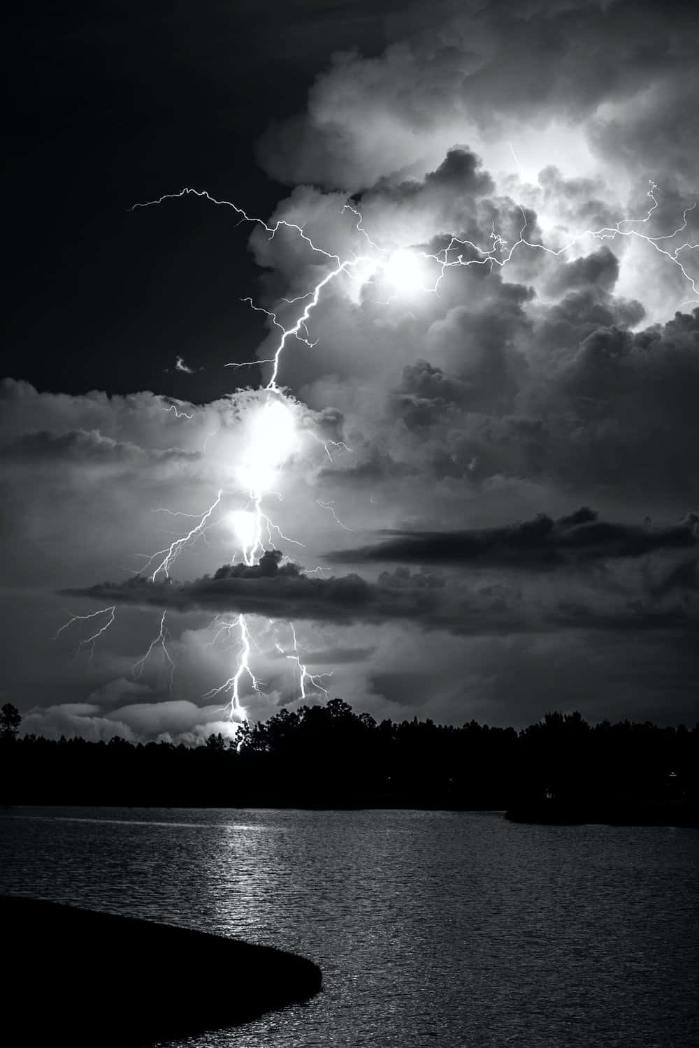 Black And White Storm 桌布 壁紙 — 一道戲劇性的黑白閃電照亮了平靜湖面上暴風雨的天空，樹木呈現剪影。
