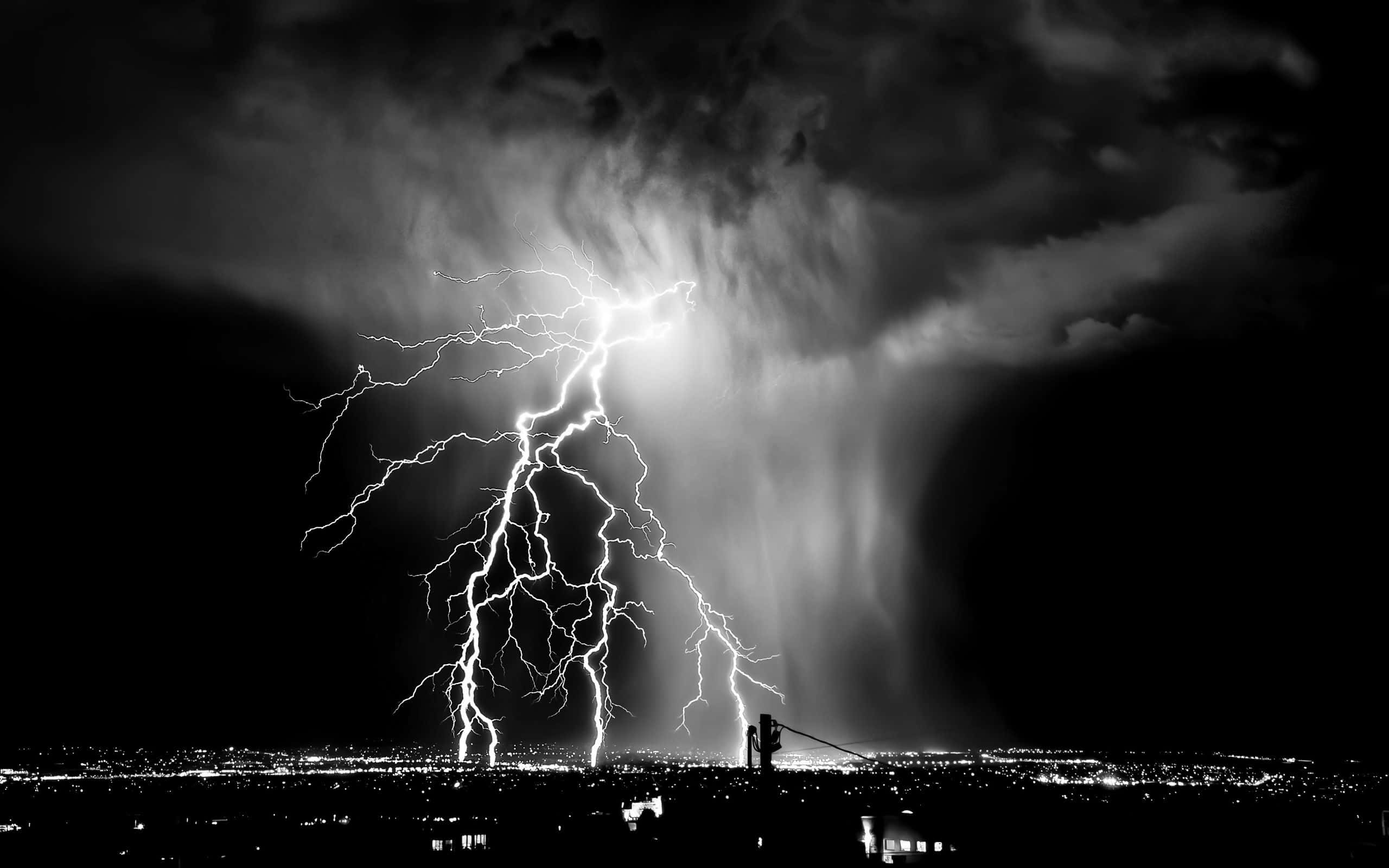 Dark Storm 桌布 壁紙 — 一道戲劇性的黑白閃電照亮了廣闊城市景觀上空暴風雨的夜空。