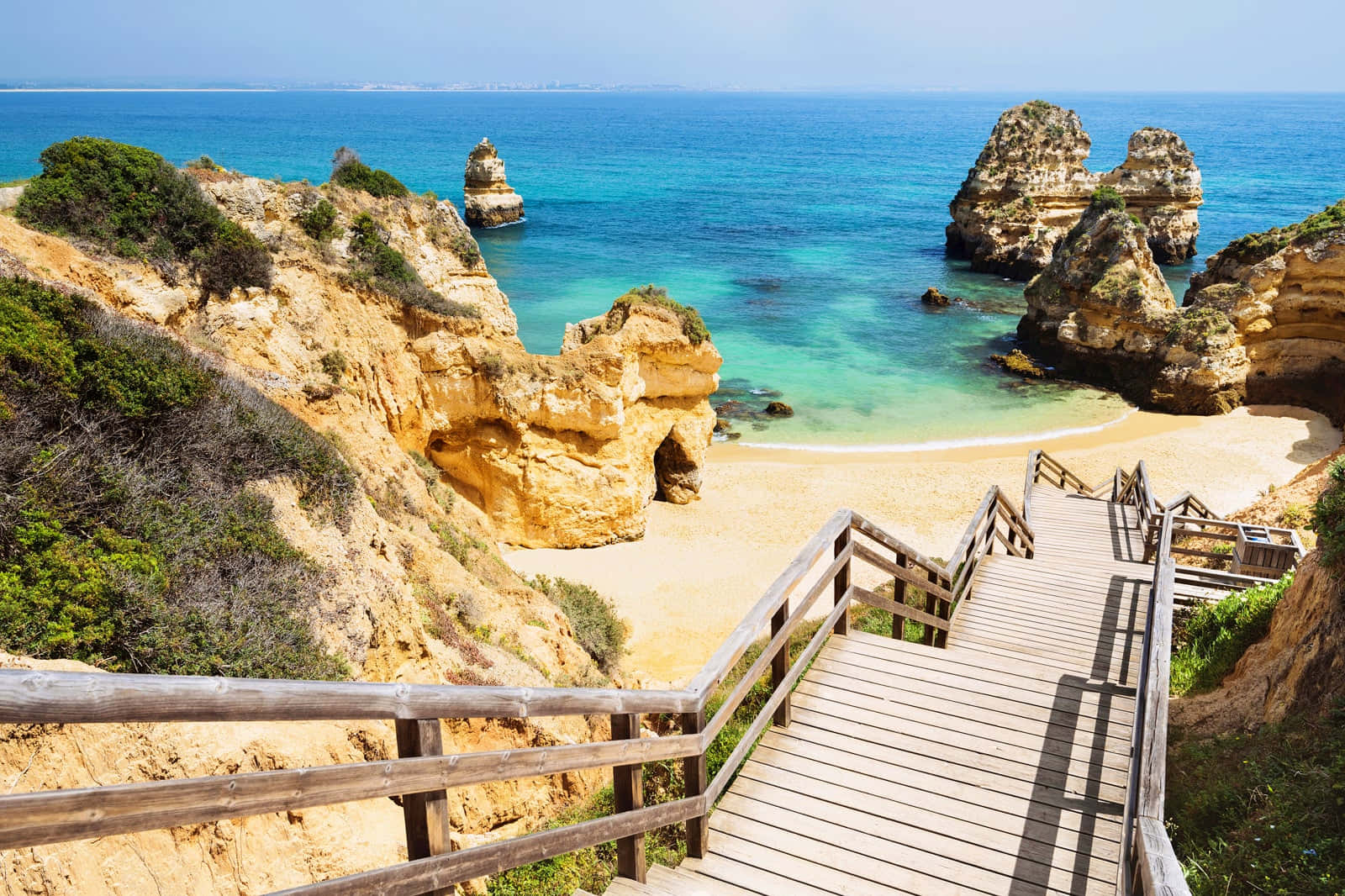 Portuguese Beach 桌布 壁紙 — 一道木樓梯向下通往一個僻靜的沙灘，四周環繞著金色懸崖、碧綠海洋和岩石地貌。