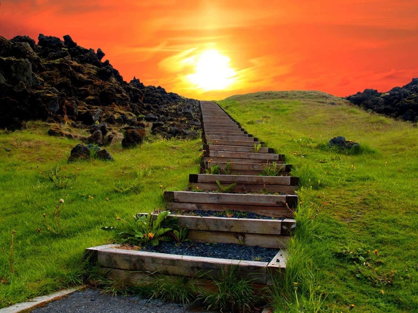 Stairway To Heaven 桌布 壁紙 — 一道木樓梯沿著草坡向上延伸，通往被深色火山岩環繞的熾熱橙色日落。