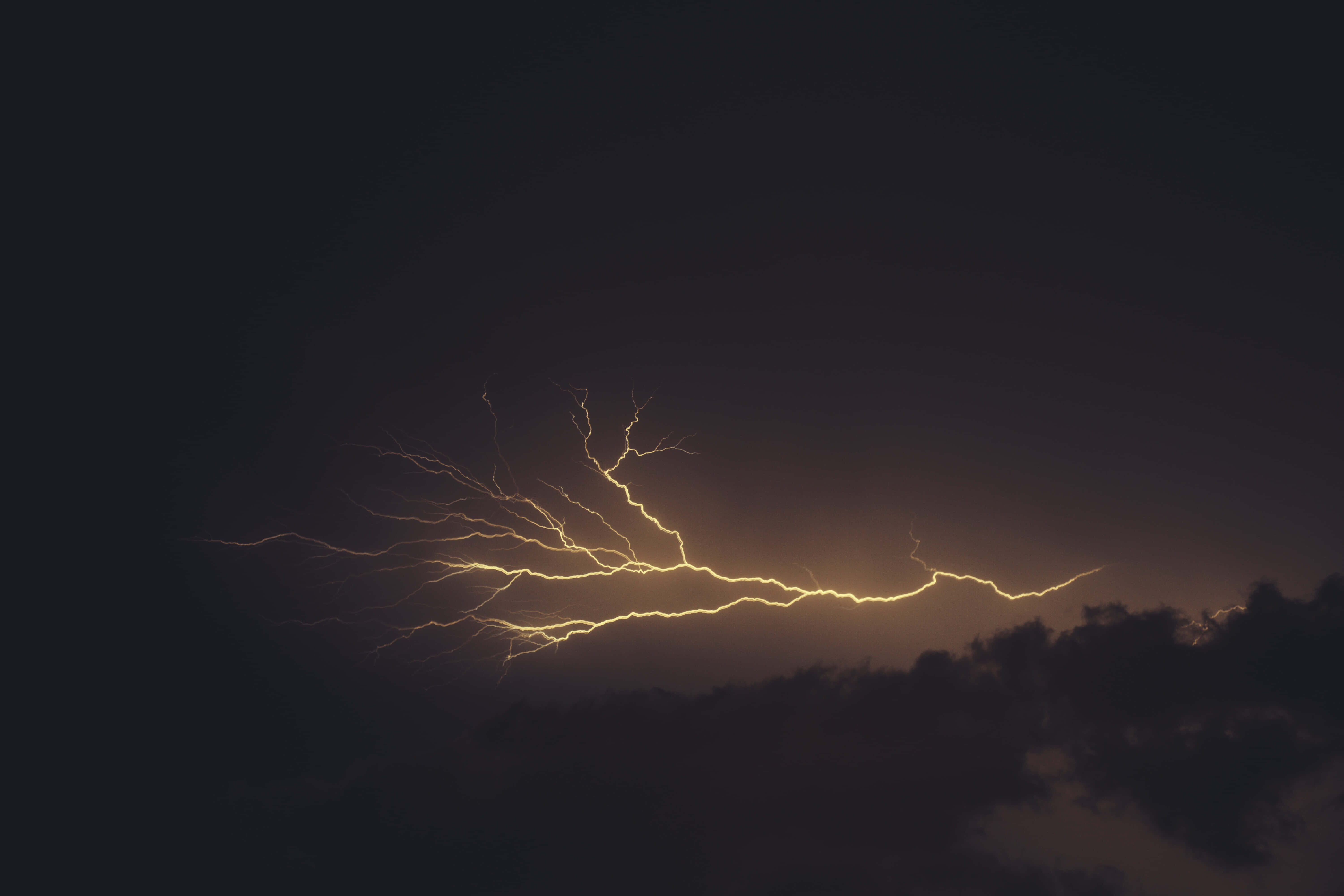 電力 桌布 壁紙 — 一道燦爛的金色閃電在黑暗暴風雨的天空中分叉，映襯著剪影般的雲層。