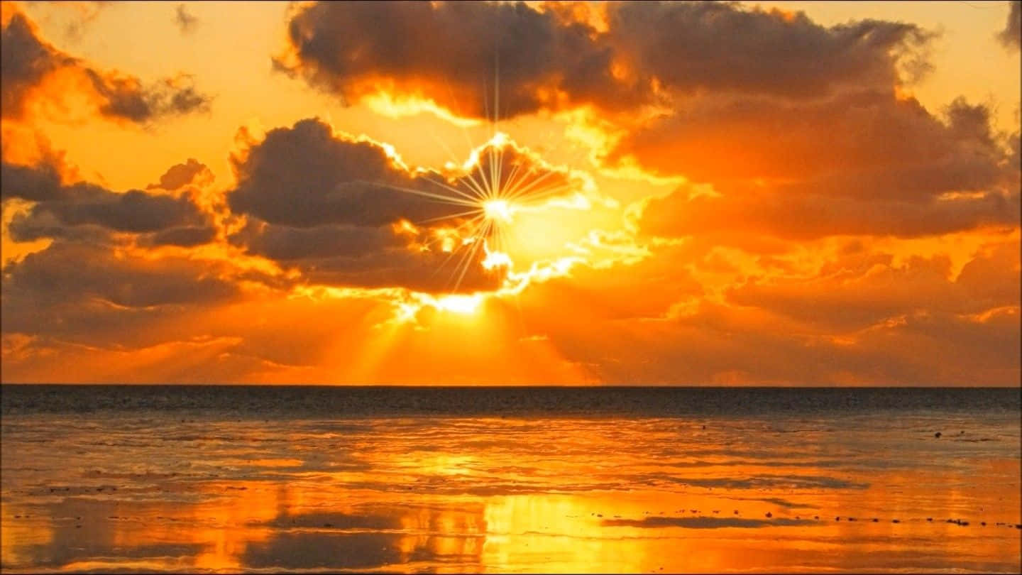 太陽 桌布 壁紙 — 一道燦爛的陽光穿透戲劇性的橙色雲層，照耀在平靜的海面上，反射出金色的光芒。