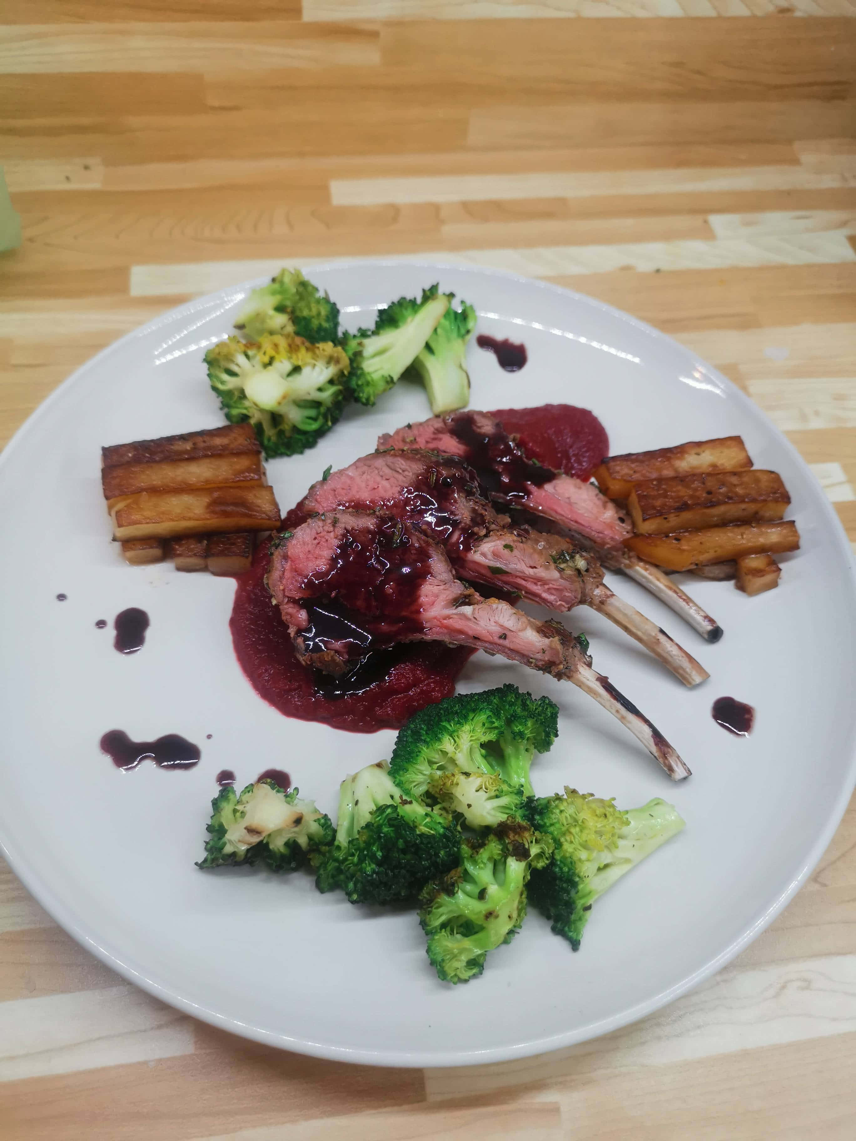 Beautiful Food 桌布 壁紙 — 一道精美擺盤的烤羊架，配以香草脆皮和紅酒肉汁，周圍環繞著烤西蘭花和地瓜角，盛載於白色餐碟上。