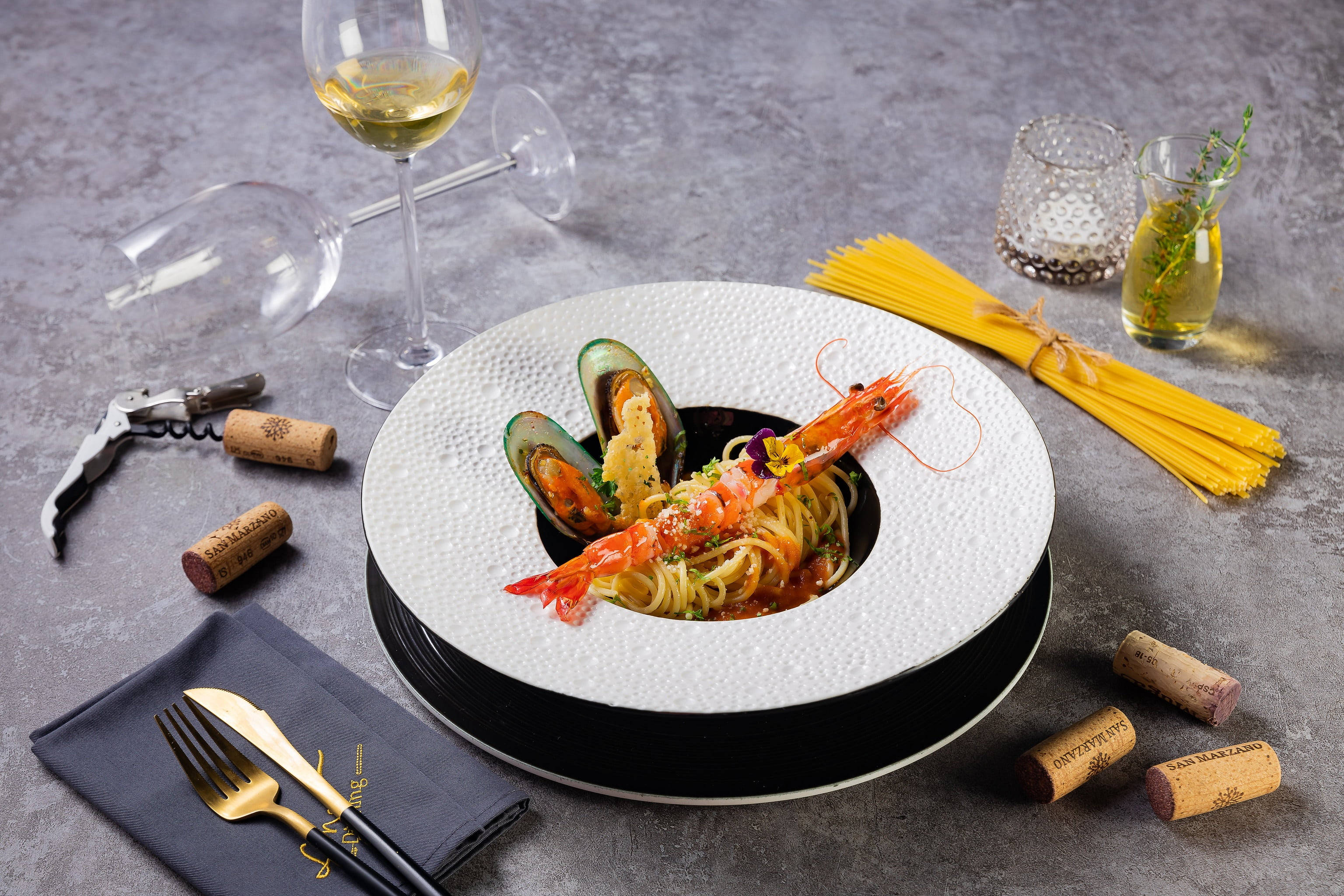 Food Photography 桌布 壁紙 — 一道美食海鮮義大利麵，搭配蝦子和淡菜，優雅地擺放在有紋理的白色碗中，周圍環繞著酒杯、軟木塞和新鮮義大利麵。