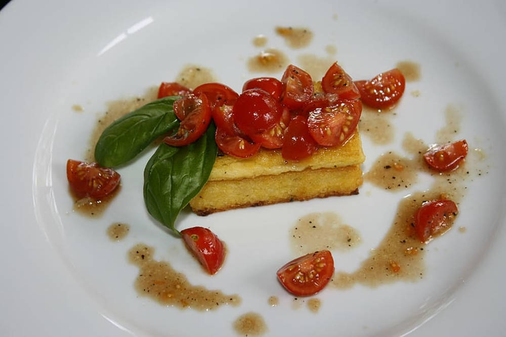 tomato 桌布 壁紙 — 一道美食菜餚，金黃色的玉米糕上點綴著鮮豔的櫻桃番茄和新鮮羅勒葉，盛放在白色盤子上。