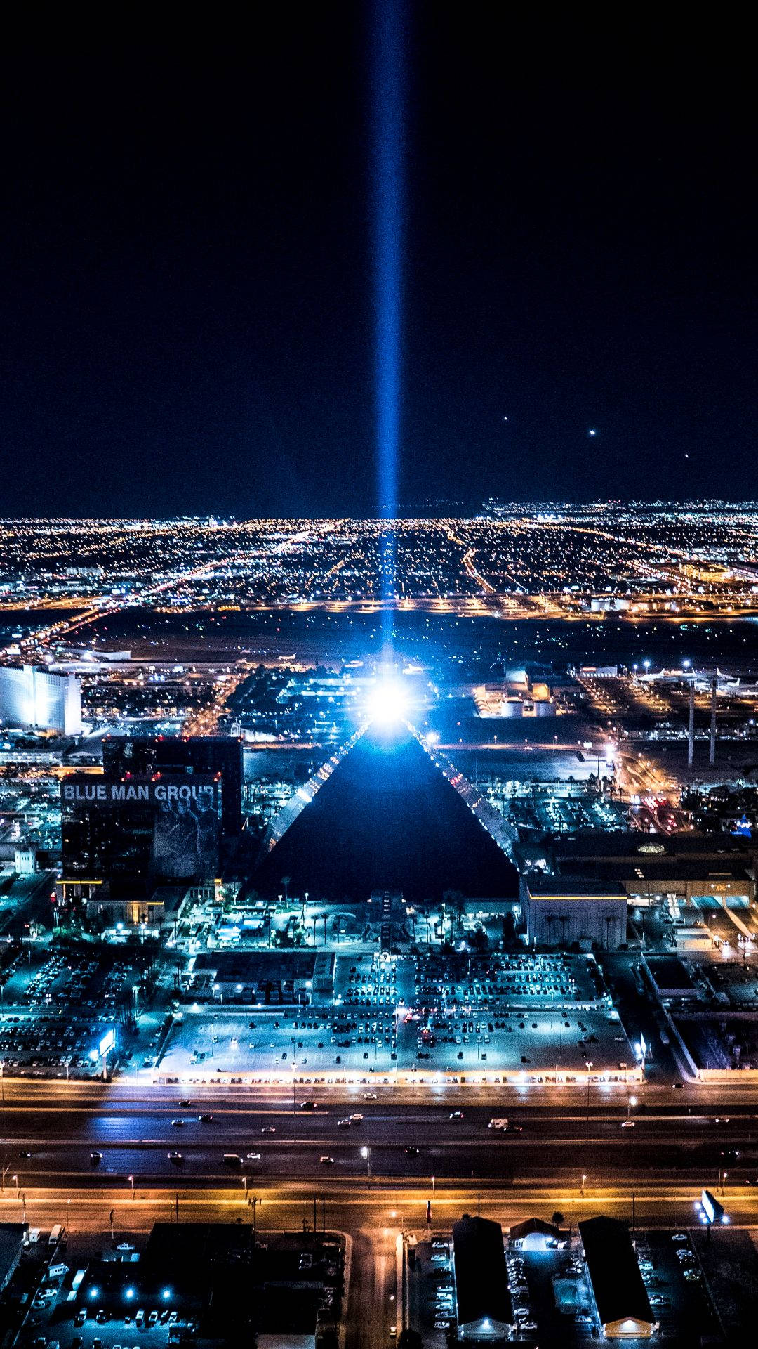 Vegas iPhone 桌布 壁紙 — 一道耀眼的藍色雷射光束劃破夜空，照亮了下方廣闊的城市景觀，街道和建築物閃爍著光芒。