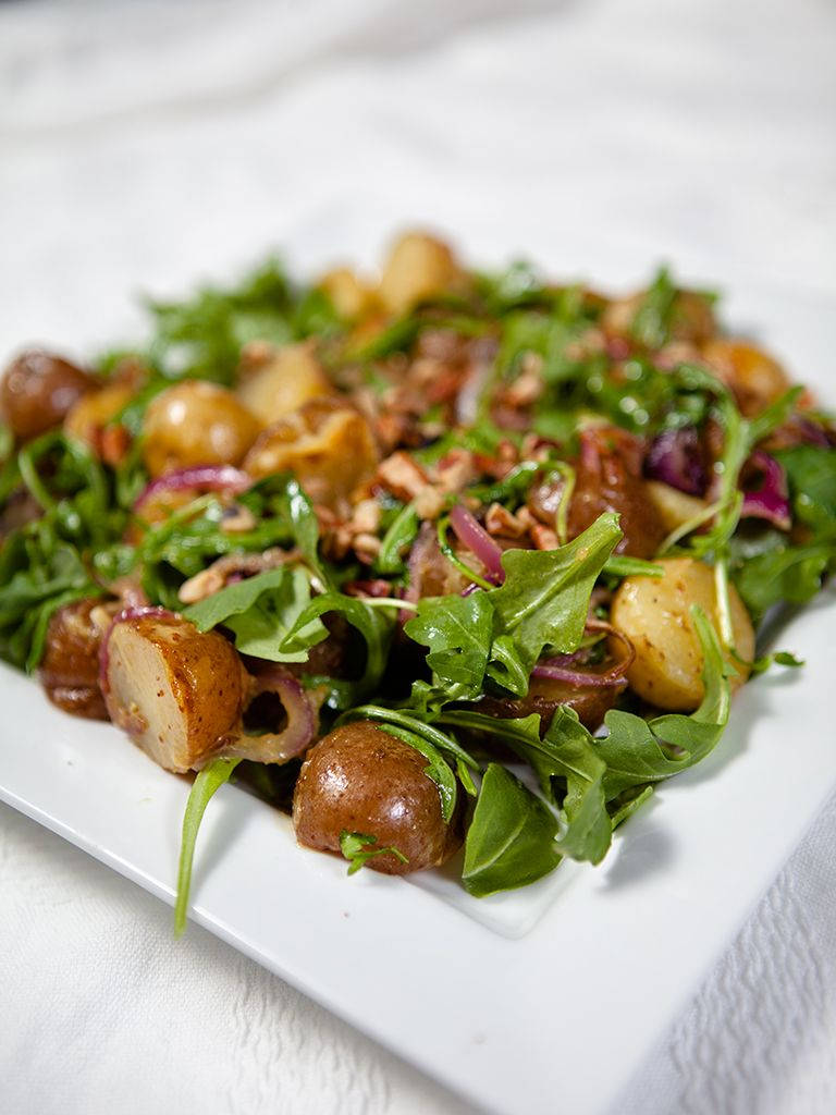 Arugula 桌布 壁紙 — 一道色彩繽紛的沙拉，包含烤馬鈴薯、芝麻葉、紅洋蔥和核桃，盛放在白色盤子上。