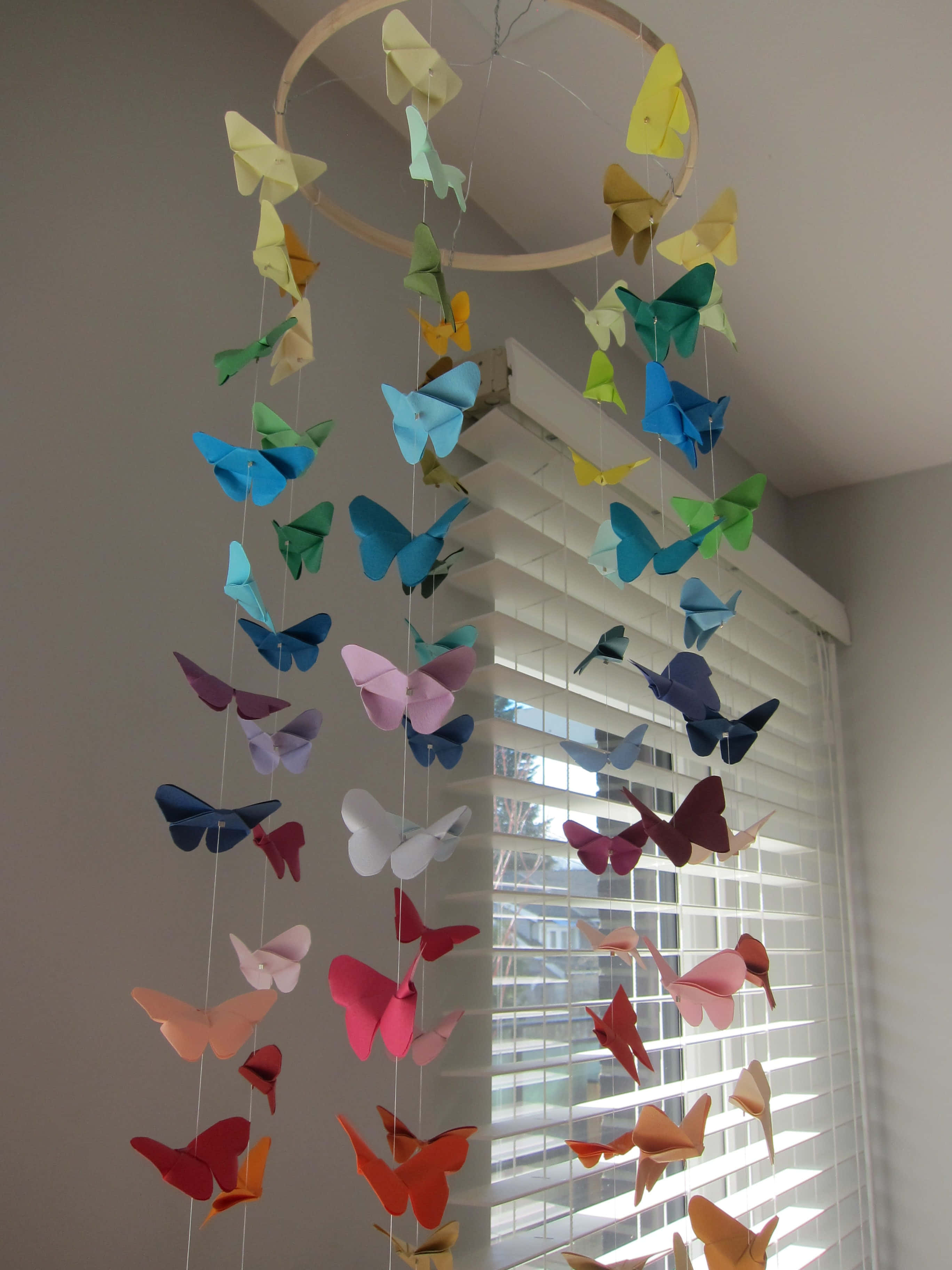 Butterfly Origami 桌布 壁紙 — 一道色彩繽紛的紙蝴蝶彩虹掛在窗邊的木環上，窗戶裝有百葉窗。