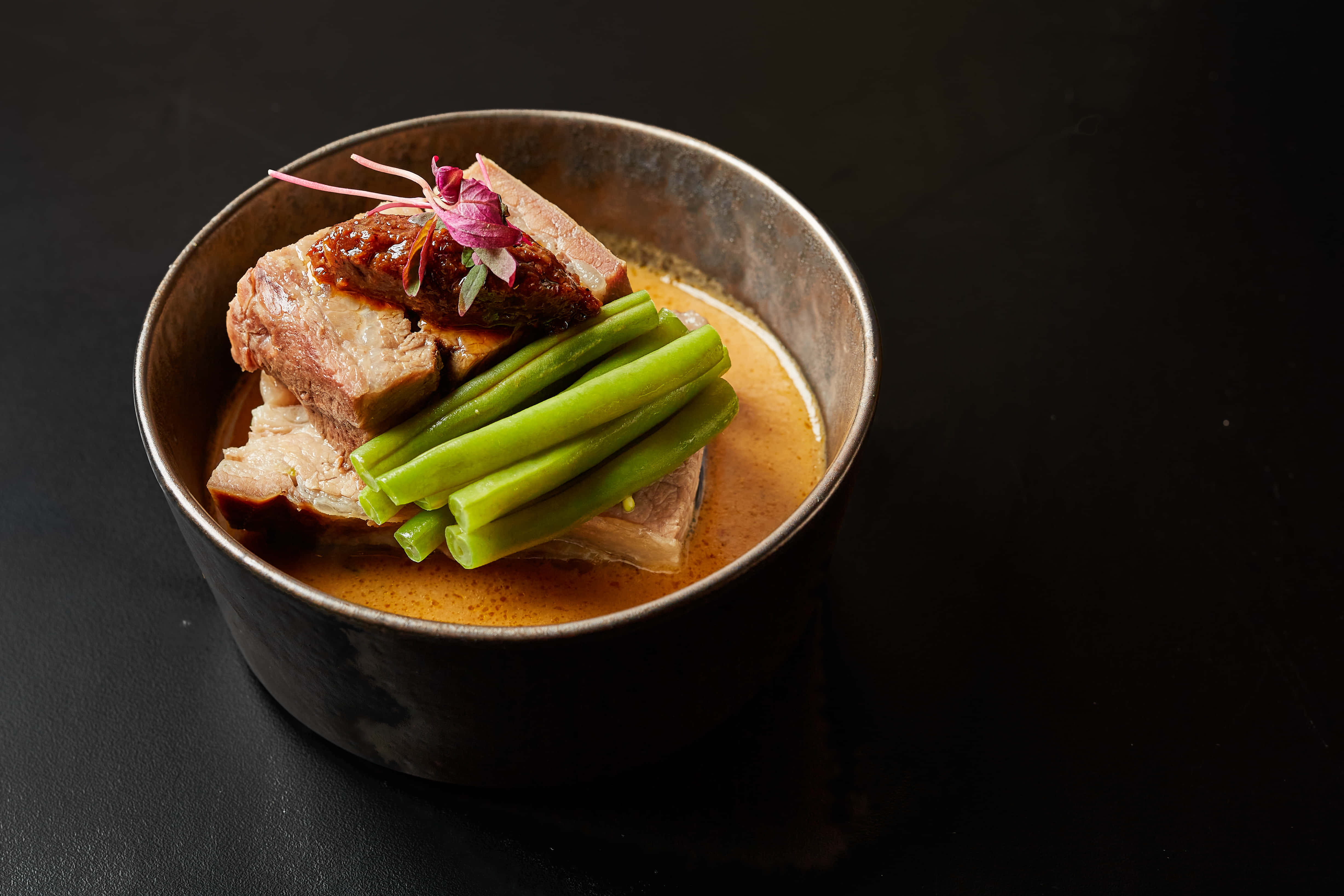 Vegetables 桌布 壁紙 — 一道豐富的釉面豬肉菜餚，搭配青豆和食用花卉，放在質樸的金屬碗中，背景為深色。