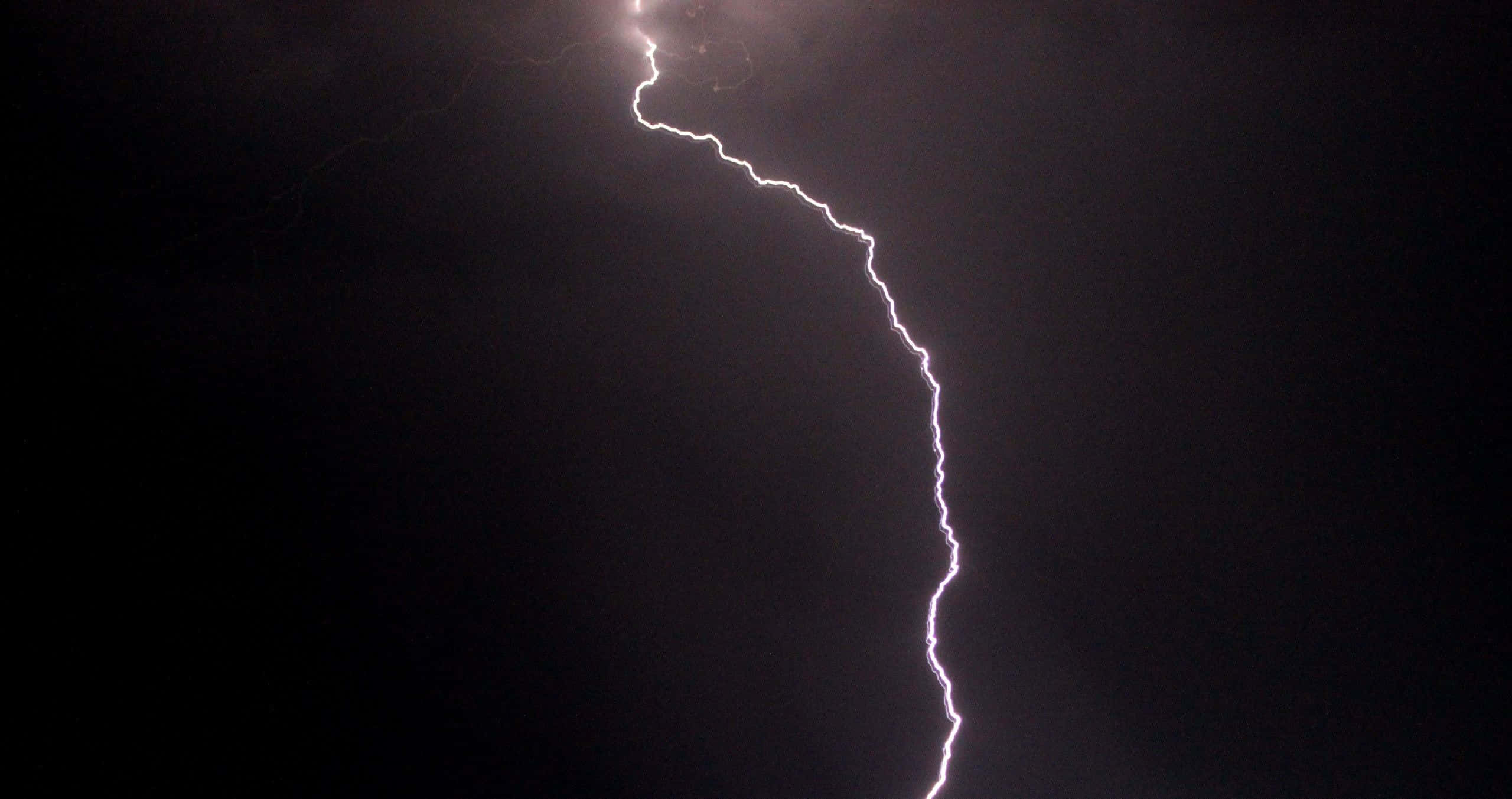 thunder 桌布 壁紙 — 一道鋸齒狀的閃電在漆黑的暴風雨天空中叉開，帶有強烈的白色和紫色色調。