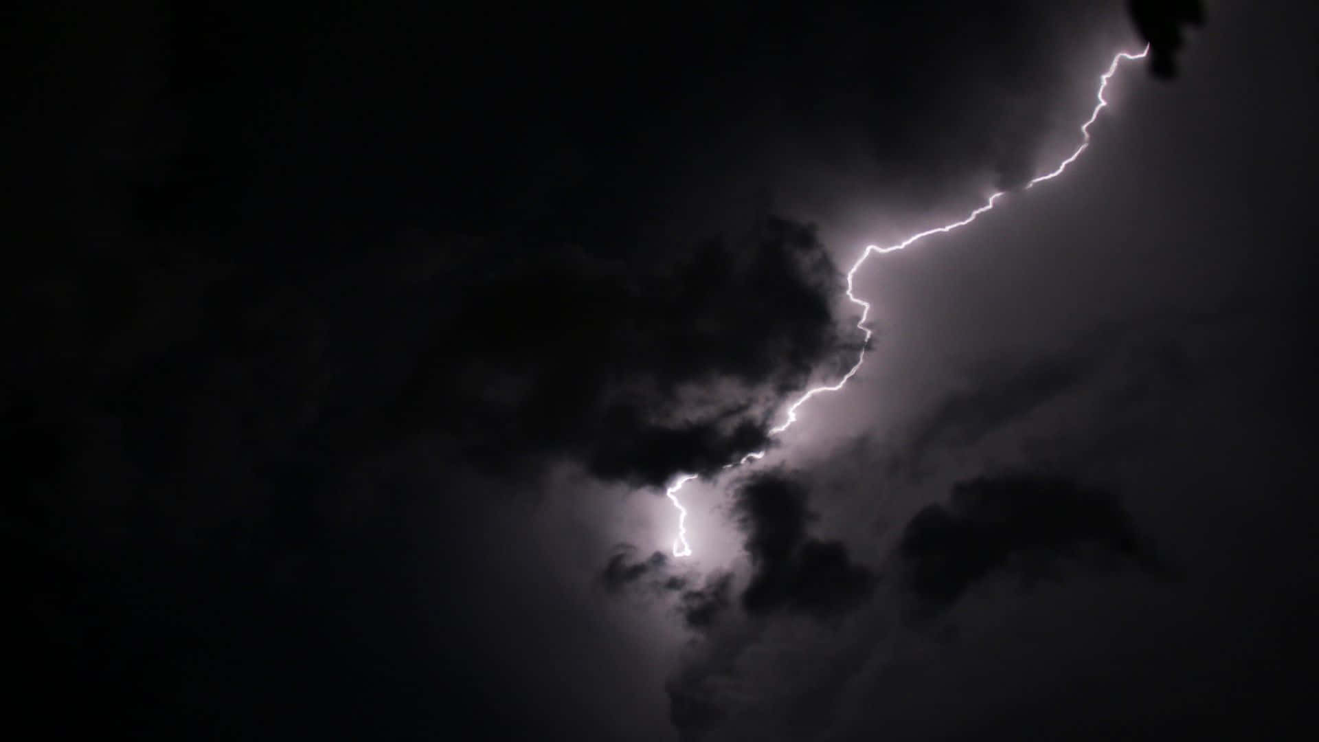 黑夜 桌布 壁紙 — 一道鋸齒狀閃電劃破黑暗的暴風雨天空，照亮了旋轉的雲層，構成戲劇性的夜間景象。