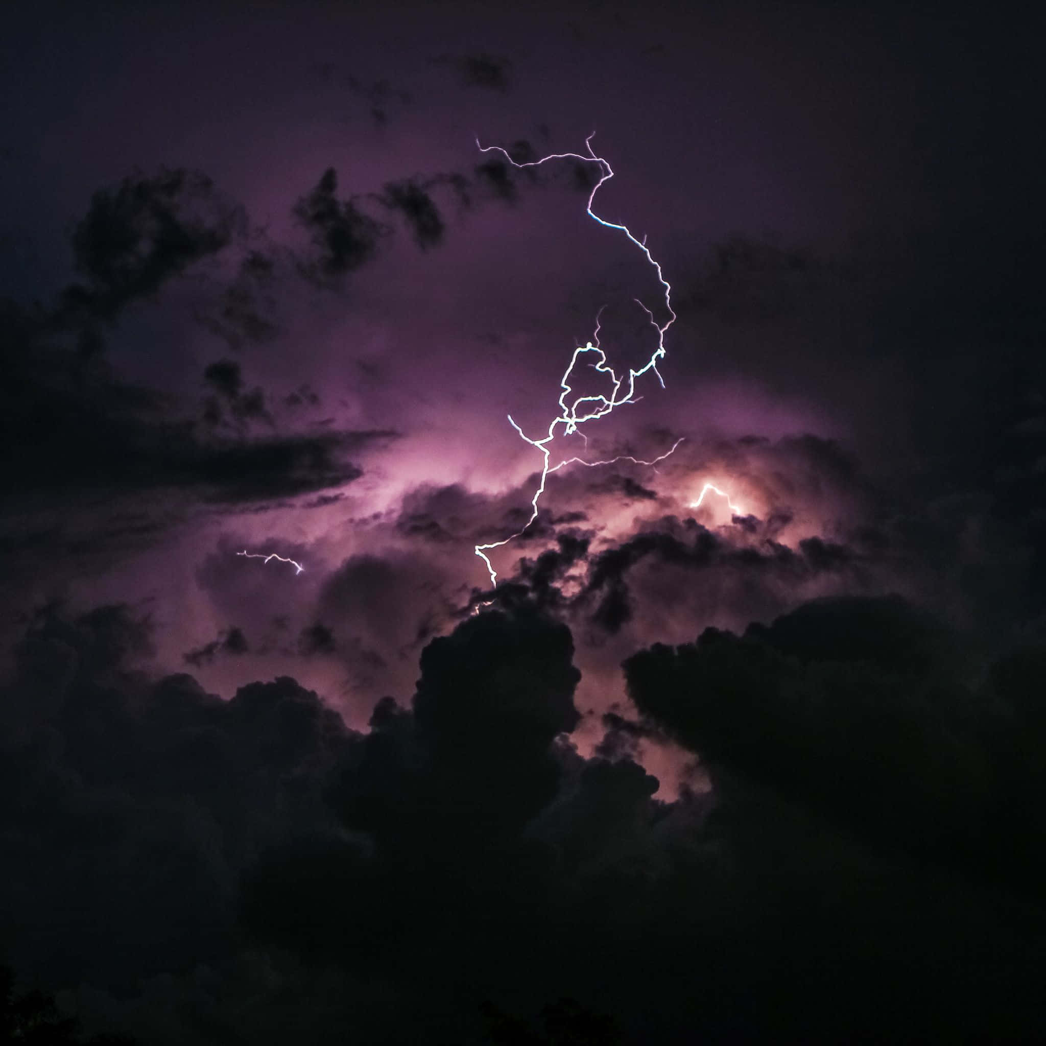 夜空 桌布 壁紙 — 一道鋸齒狀閃電劃過洶湧的紫色暴風雨天空，照亮密集的雲層，形成戲劇性的夜景。