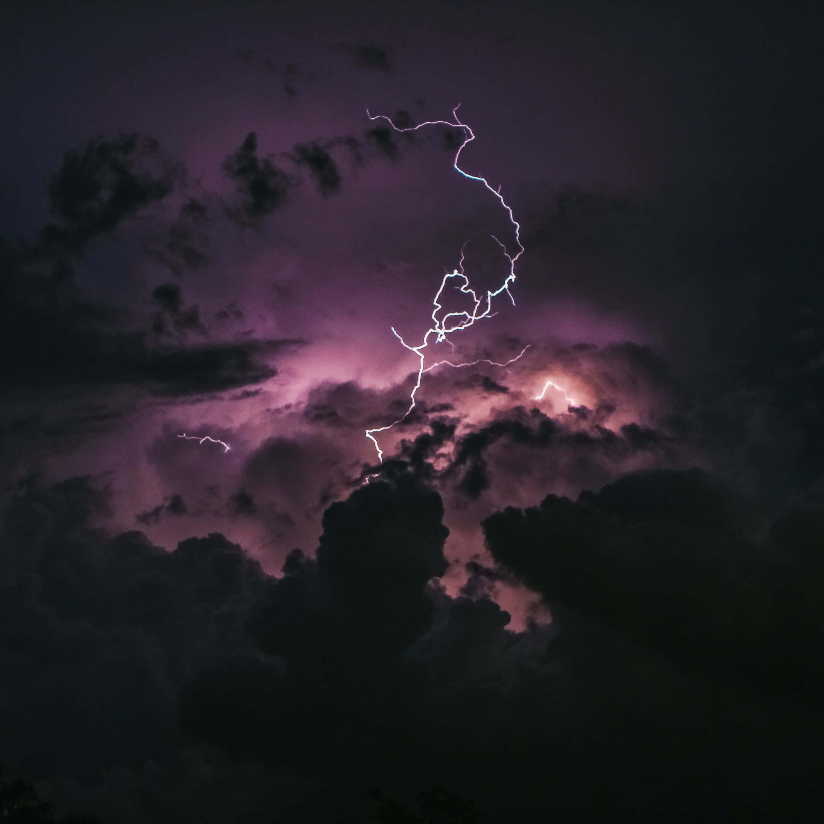 Dark Sky 桌布 壁紙 — 一道鋸齒狀閃電在洶湧的紫色暴風雨天空中分叉，照亮濃密的雲層，形成戲劇性的夜間景象。