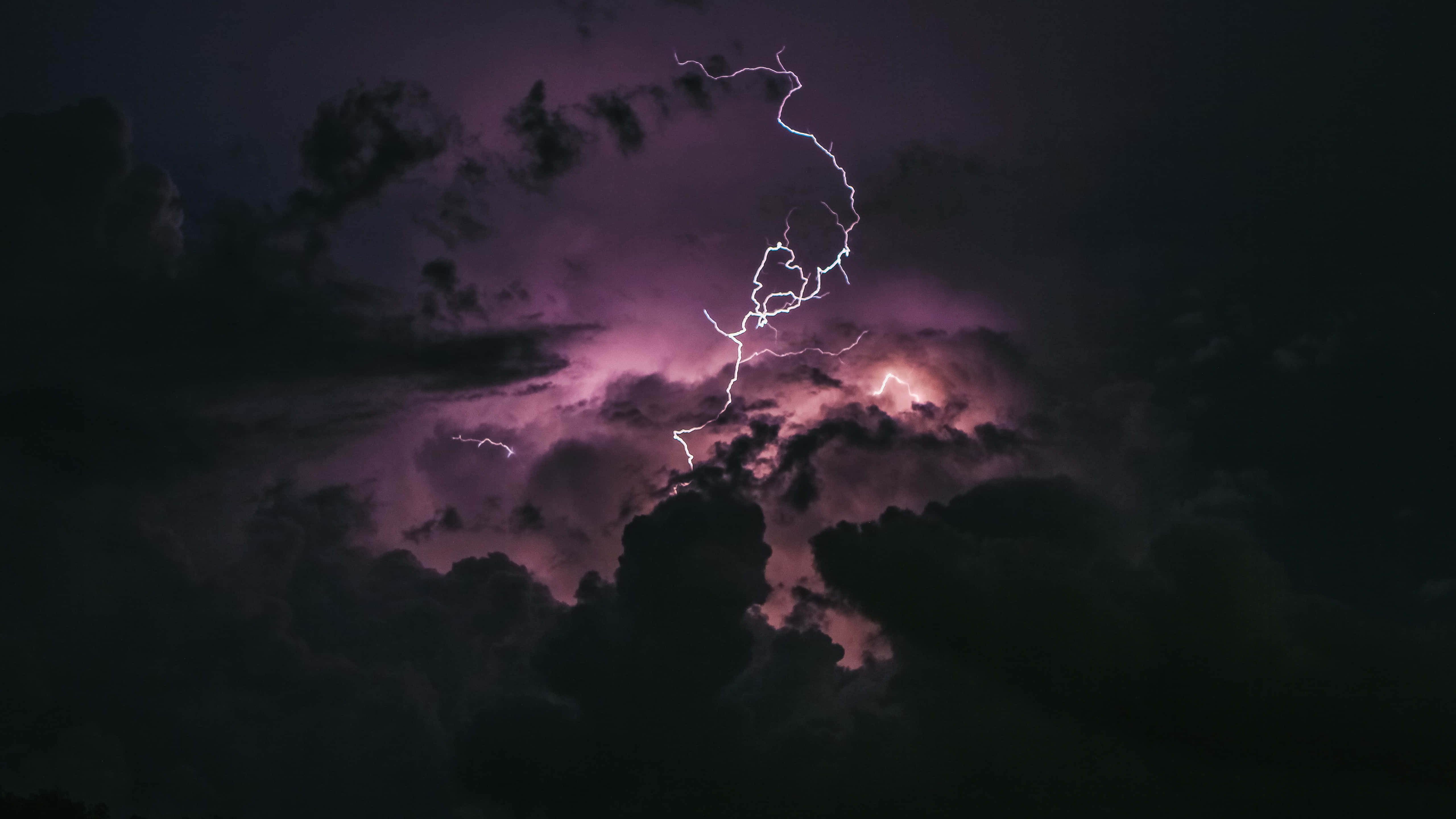 Clouds 4K 桌布 壁紙 — 一道鋸齒狀閃電在翻騰的紫色和黑色暴風雨天空中分叉。