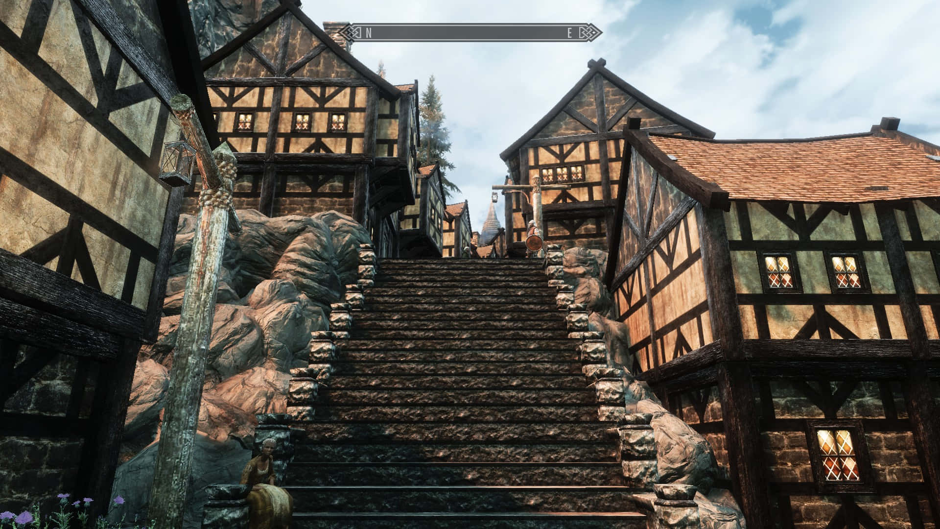 Skyrim Solitude 桌布 壁紙 — 一道陡峭的石階在明亮的藍天和散落的雲朵下，於中世紀半木結構房屋之間向上延伸。
