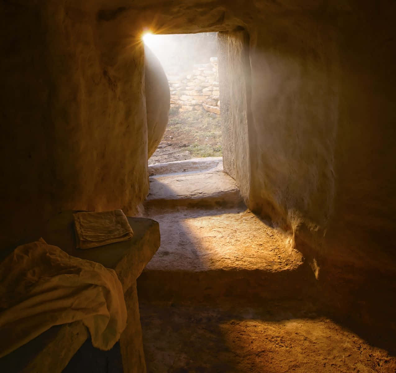 Empty Tomb 桌布 壁紙 — 一道陽光穿過石門，照亮了簡樸洞穴住所內的灰塵和古老的粗糙石牆。