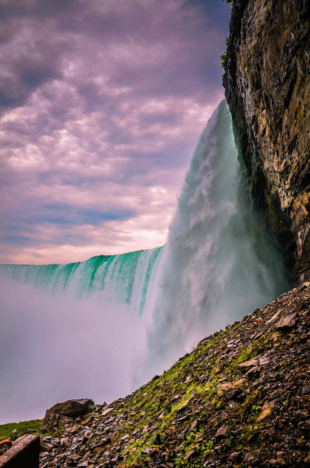 720p Niagara Falls 桌布 壁紙 — 一道雄偉的瀑布在戲劇性的紫色和粉紅色天空下，強而有力地從懸崖上傾瀉而下。
