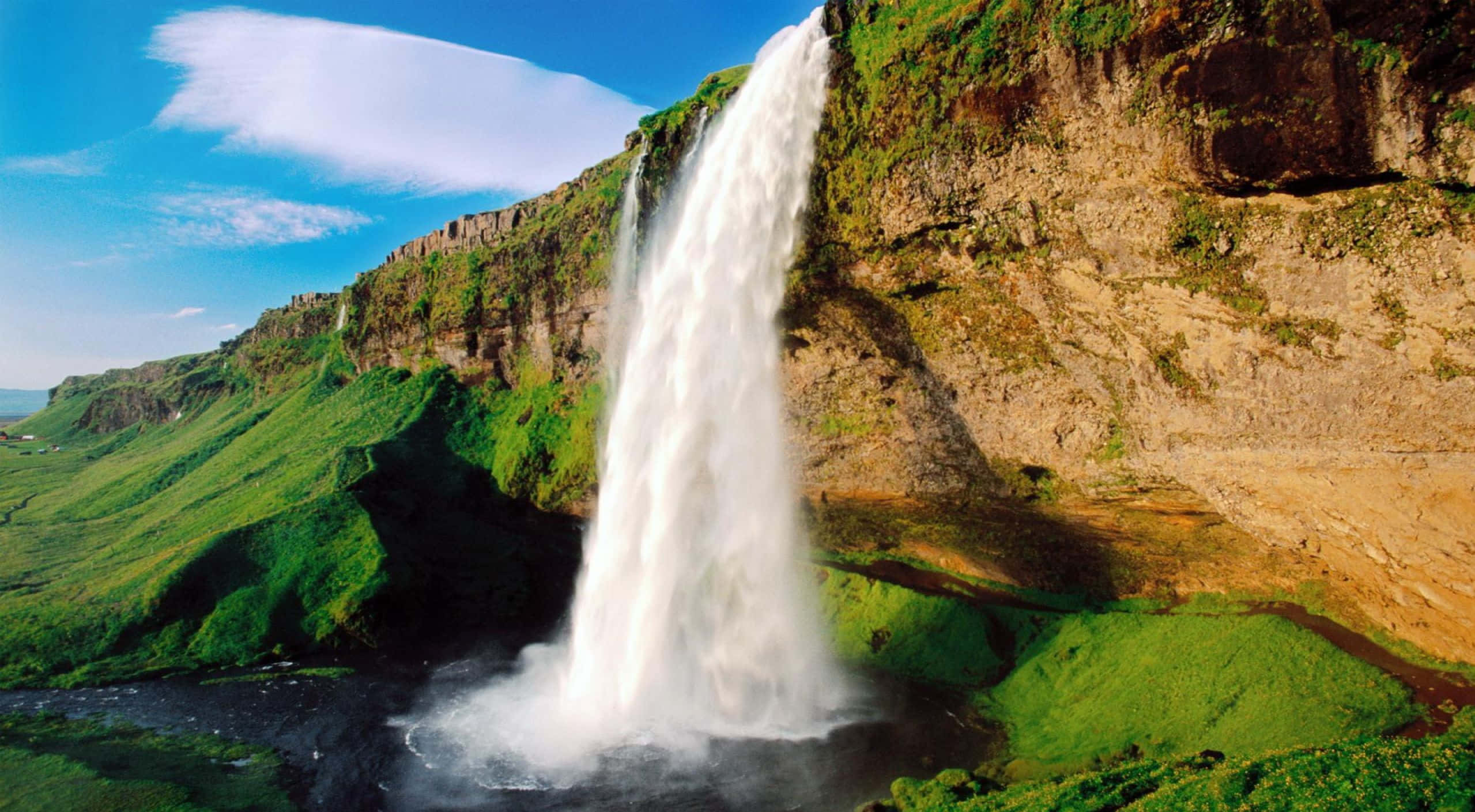 3d Waterfall 桌布 壁紙 — 一道雄偉的瀑布從崎嶇的懸崖傾瀉而下，落入煙霧繚繞的水潭，四周是蒼翠的山谷，上方是明亮的藍天。