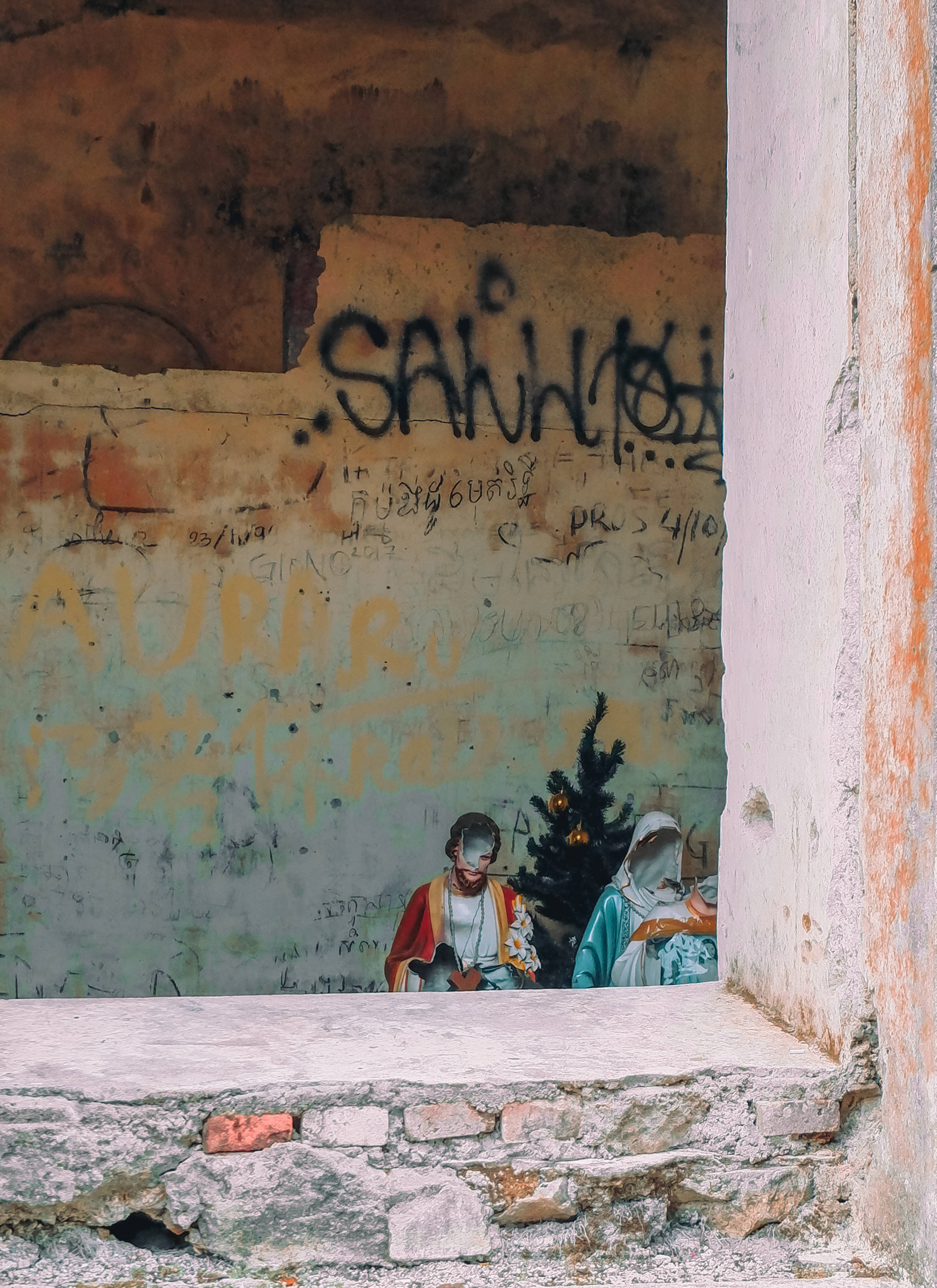 Cambodia 桌布 壁紙 — 一道飽經風霜的門口框住了一幅褪色的耶穌誕生壁畫，背景是佈滿塗鴉的牆壁。
