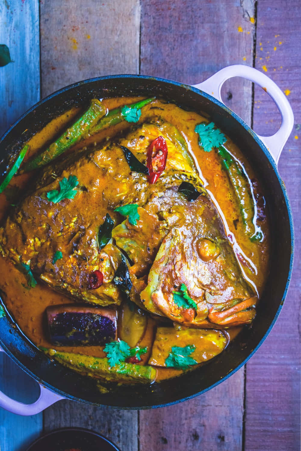 Food Photography 桌布 壁紙 — 一道香料豐富的魚咖哩，配有秋葵和辣椒，飾以香菜，放在鑄鐵鍋中，置於質樸的木桌上。