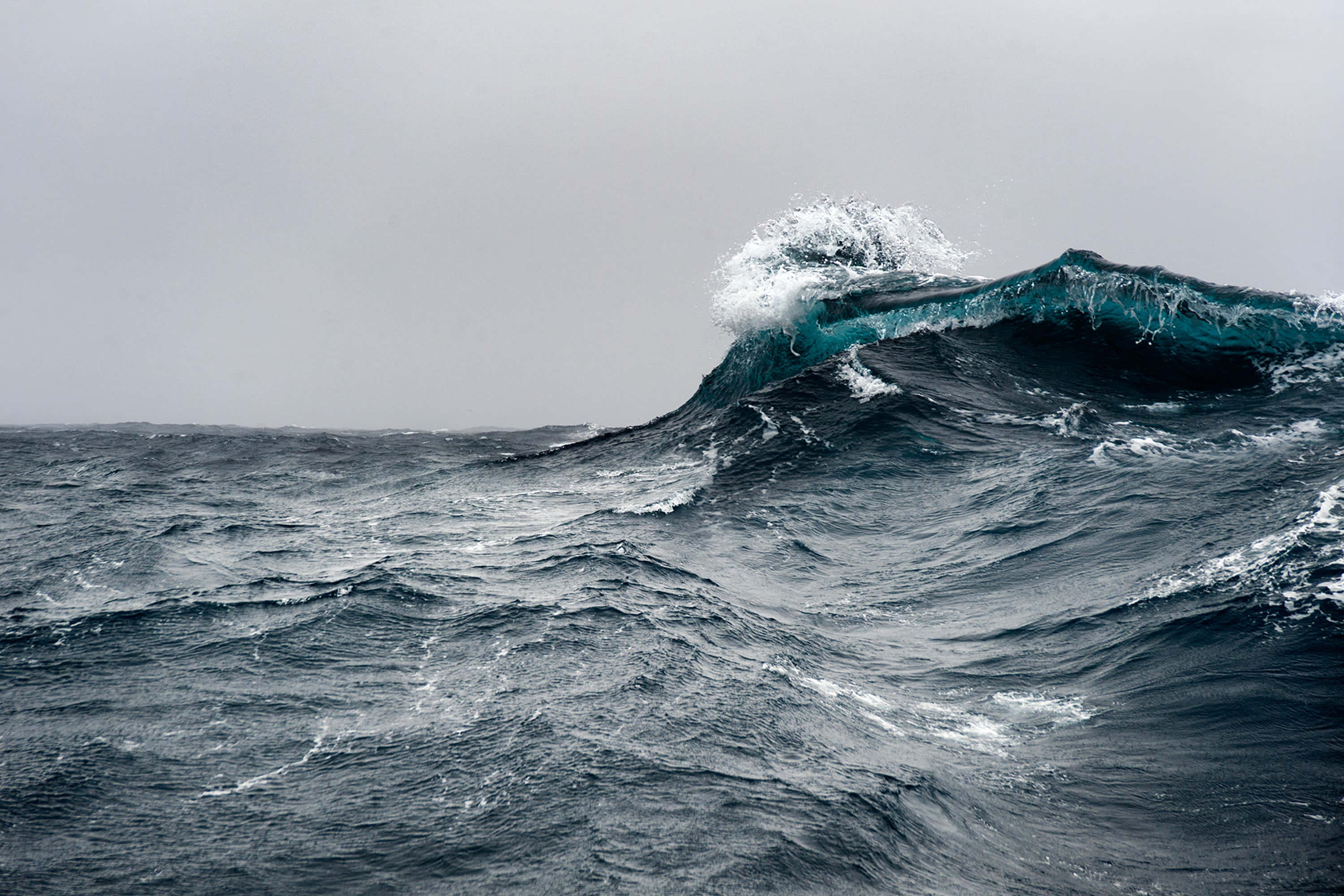 Creepy Ocean 桌布 壁紙 — 一道高聳的海浪在暴風雨的海面上翻捲，帶著泡沫般的白色浪花，映襯著灰色的天空。