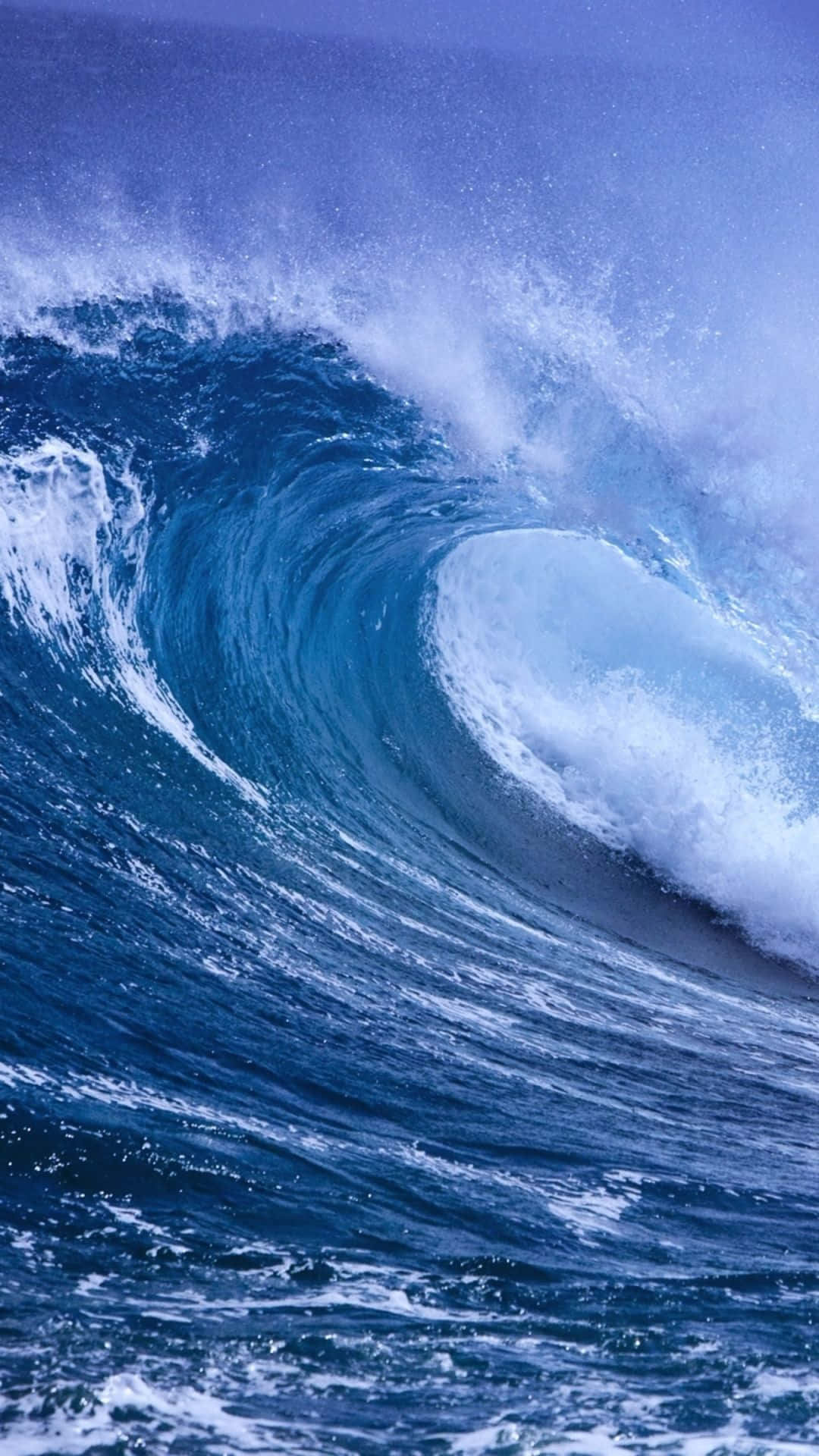 Wave 桌布 壁紙 — 一道高聳的藍色海浪捲成完美的管浪，帶著泡沫般的白色水花，映襯著深藍色的天空。