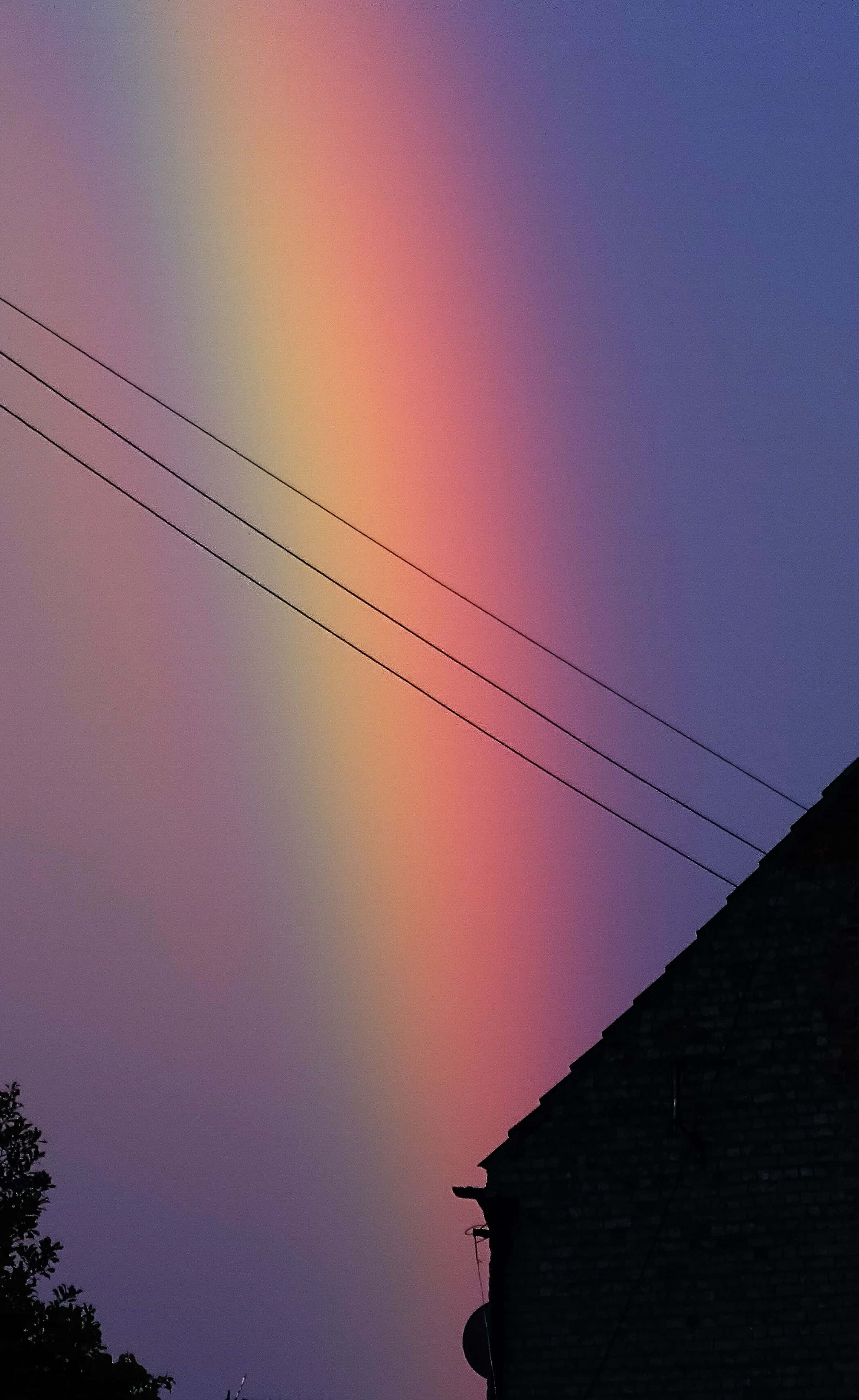 Aesthetic Rainbow Mobile 桌布 壁紙 — 一道鮮豔的彩虹橫跨在暮色天空上，下方是深色屋頂和電線。