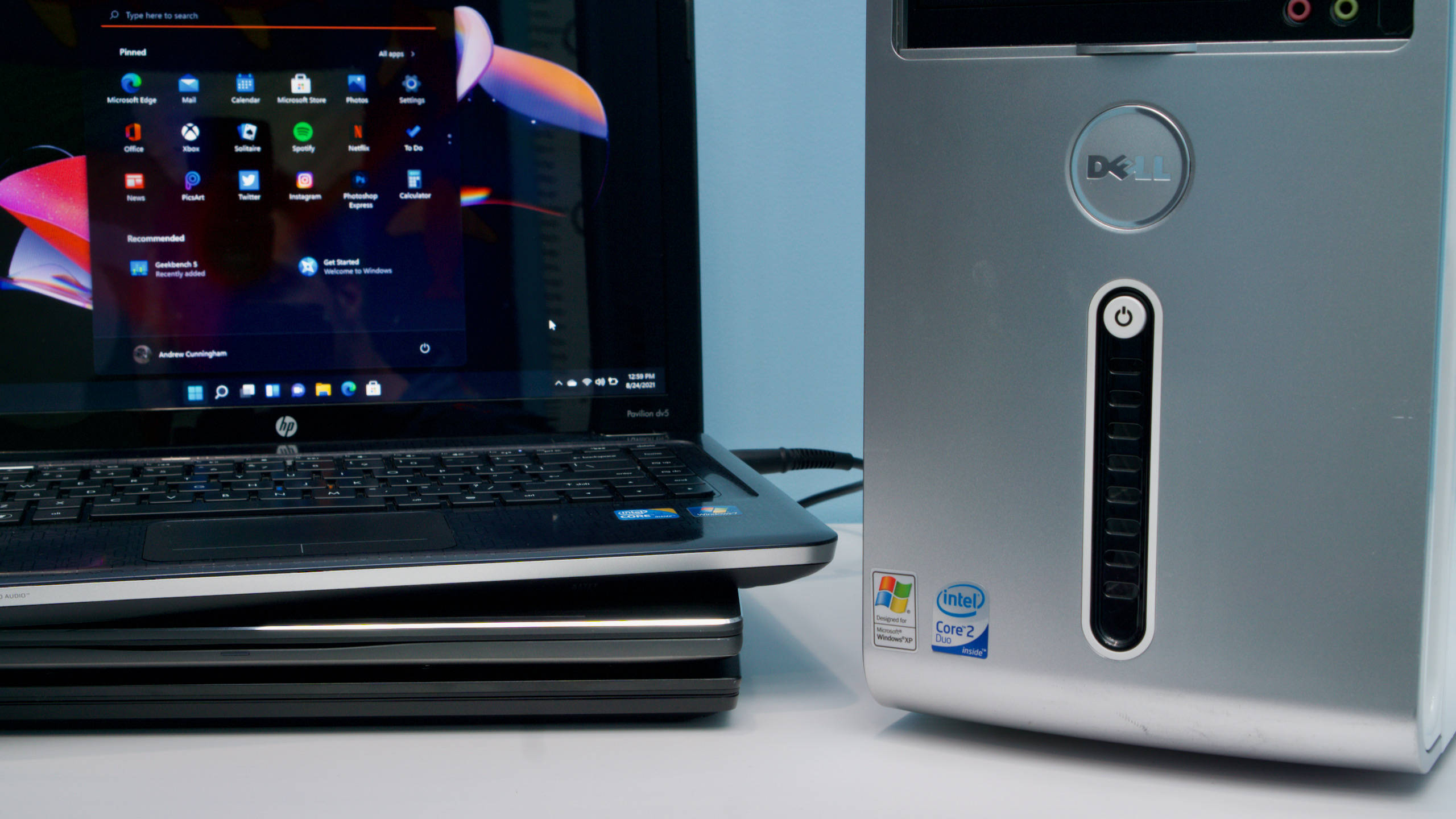 Windows 11 桌布 壁紙 — 一部 Dell 桌上型主機和一部 HP 筆記型電腦並排放在白色表面上，螢幕上顯示 Windows 開始功能表。