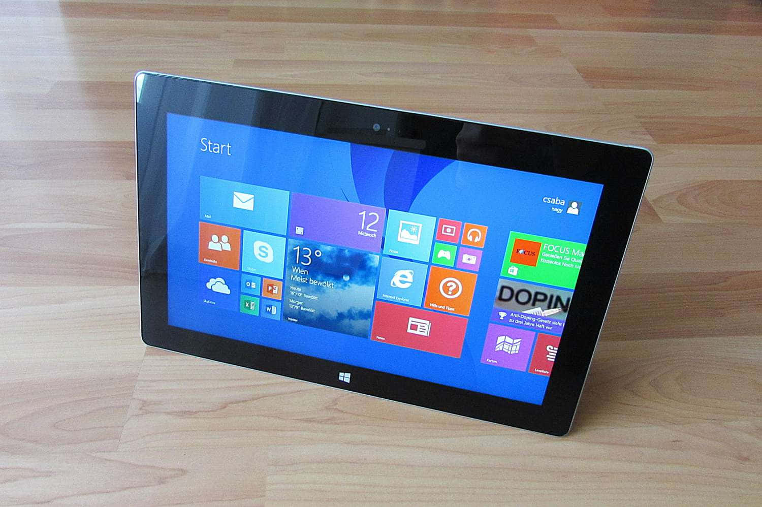 高清 桌布 壁紙 — 一部 Microsoft Surface 平板電腦顯示 Windows 開始畫面，帶有彩色方塊，放置在淺色木地板上。