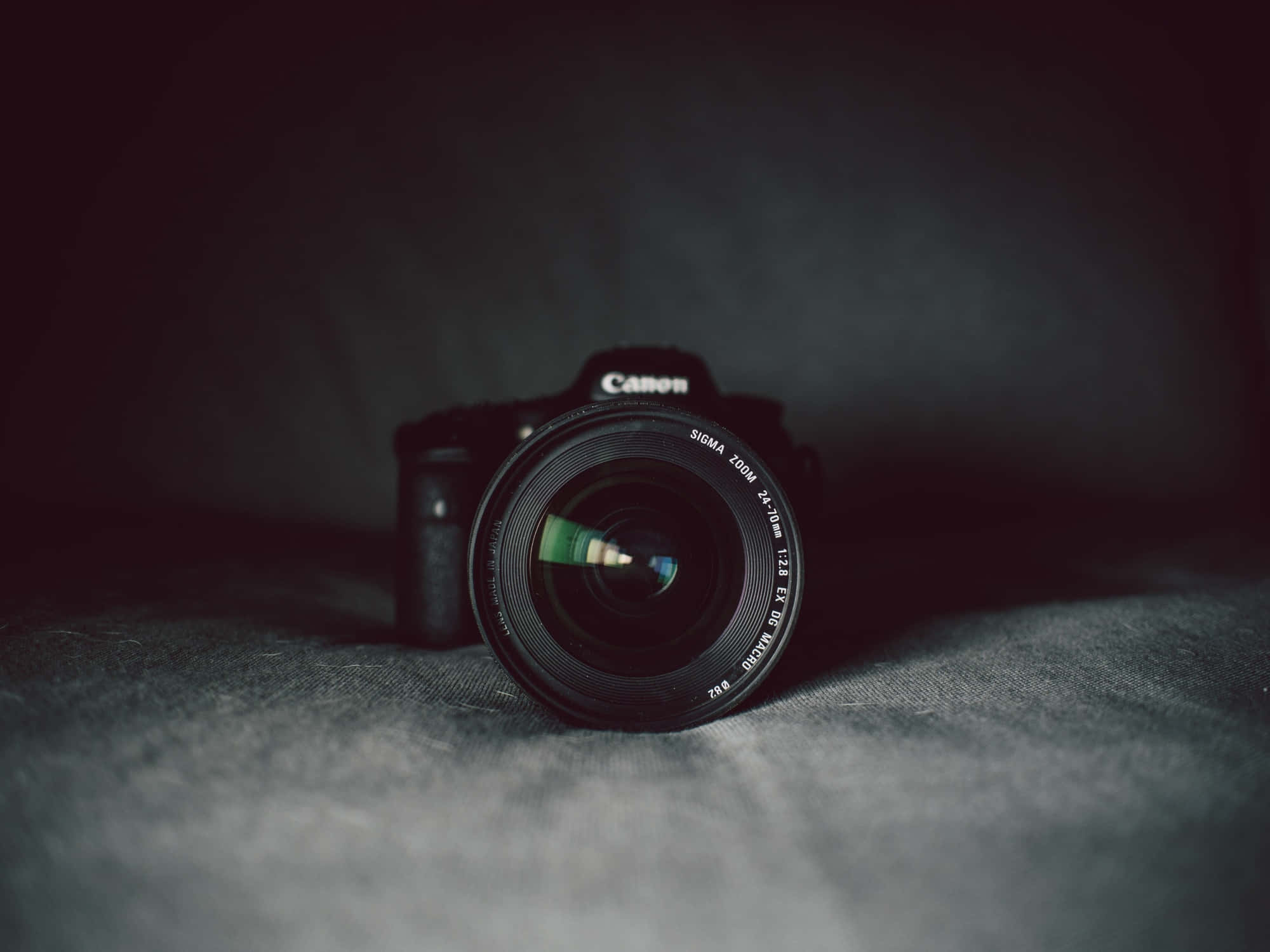 相機 桌布 壁紙 — 一部Canon DSLR相機配備Sigma鏡頭，放置在紋理灰色布料上，處於戲劇性的低光照明下。
