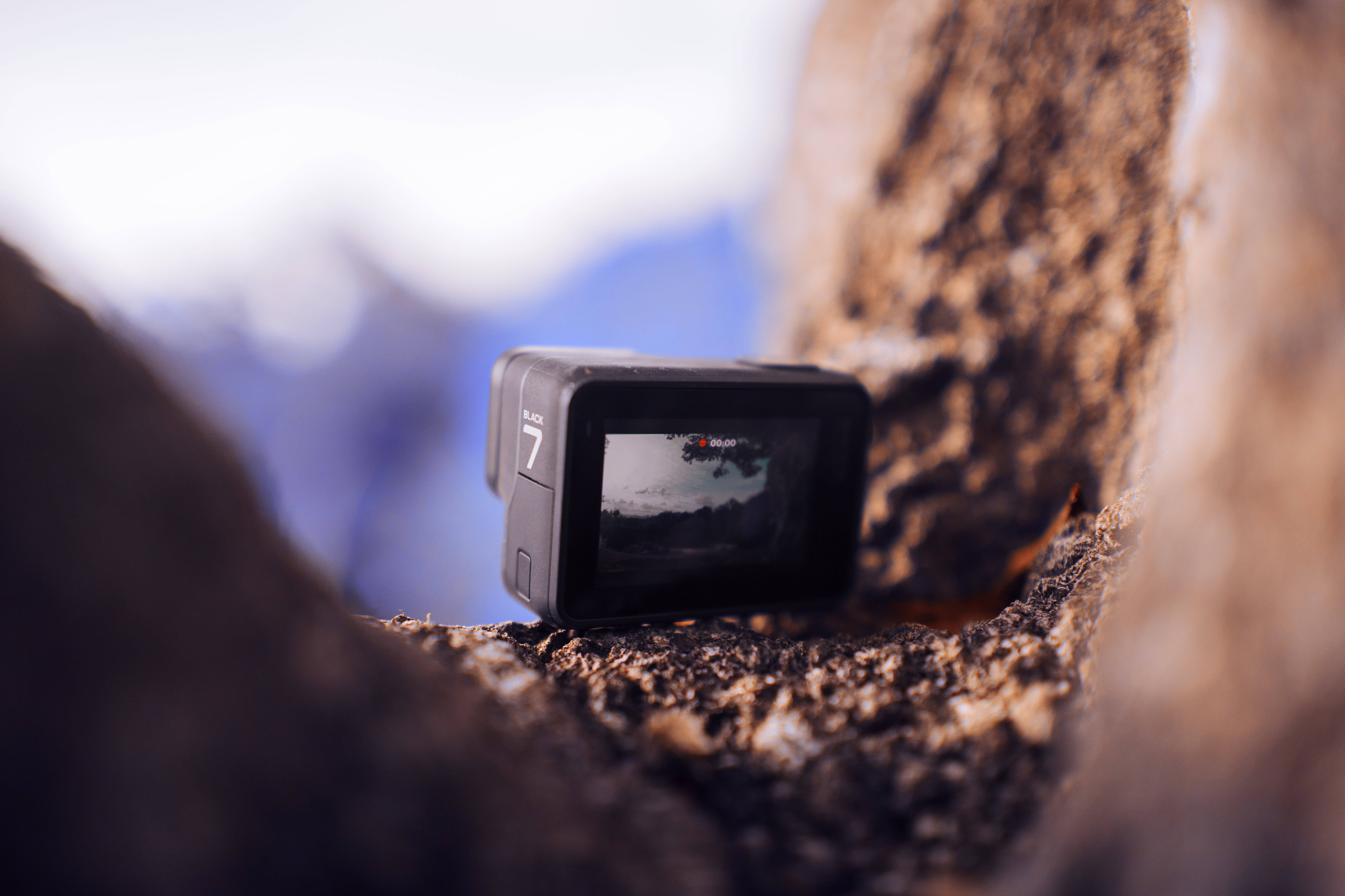 攝影 桌布 壁紙 — 一部GoPro 7相機嵌在岩石縫中，螢幕上捕捉到模糊的山景。