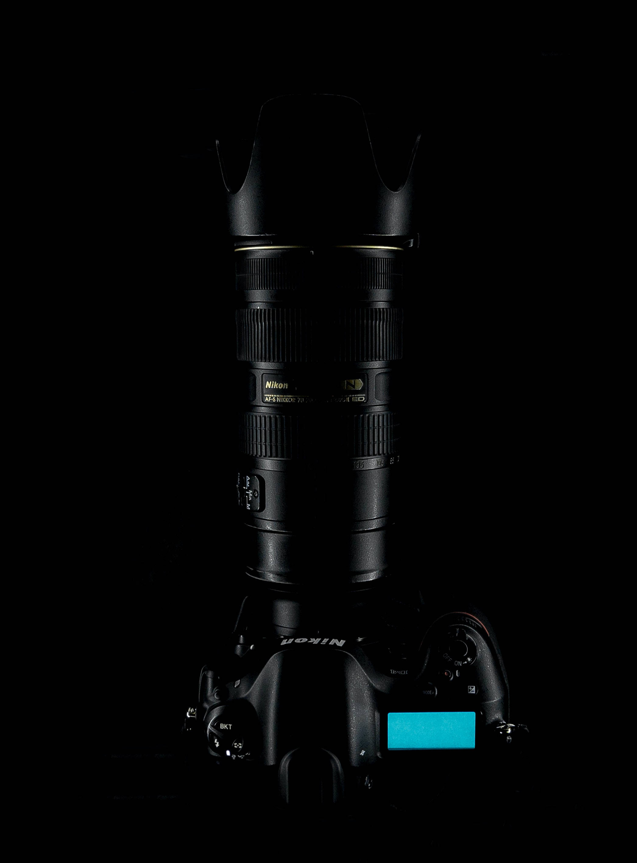 相機 桌布 壁紙 — 一部Nikon DSLR相機連鏡頭孤立在純黑色背景上，其LCD螢幕發出青色光芒。