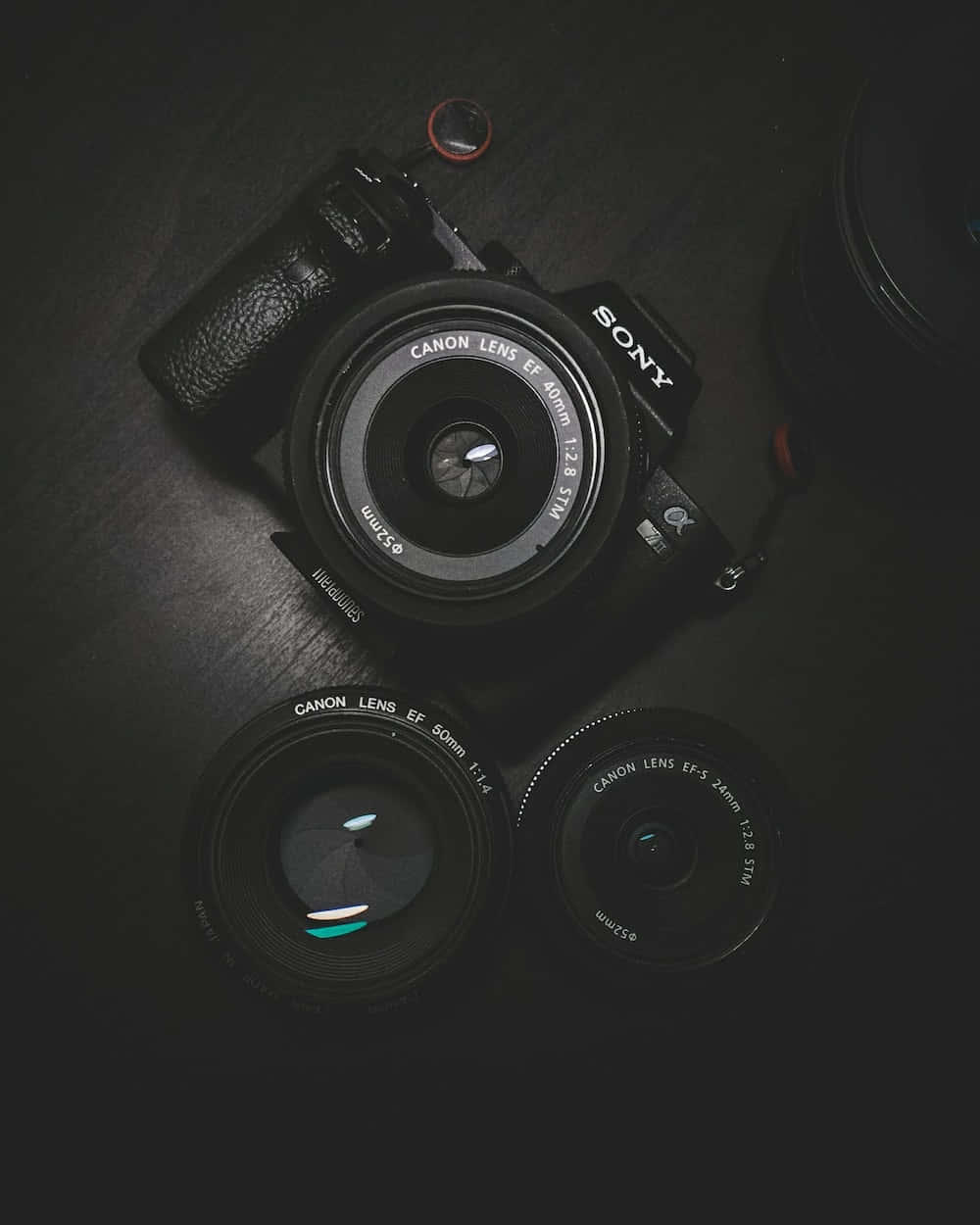 相機 桌布 壁紙 — 一部Sony相機配備Canon鏡頭，在戲劇性燈光下放置於深色表面上。