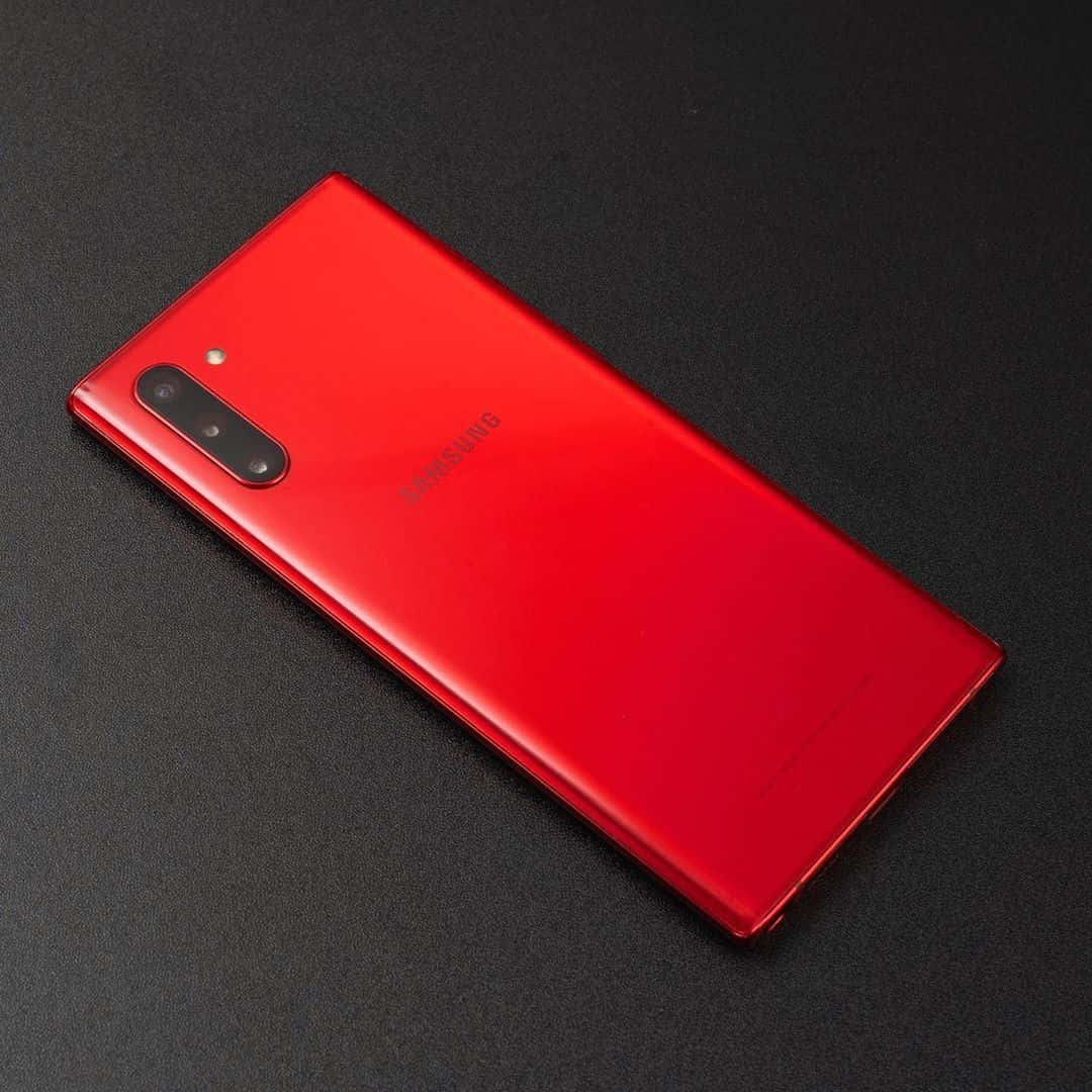 Note 10 桌布 壁紙 — 一部亮紅色Samsung智慧型手機斜放在深色紋理表面上，其相機模組和標誌清晰可見。