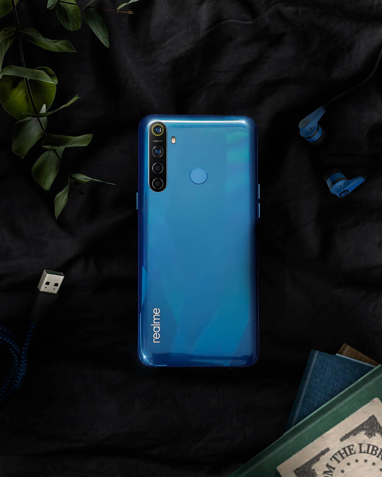 黑色布料上帶有耳塞和書本的藍色 realme 手機。