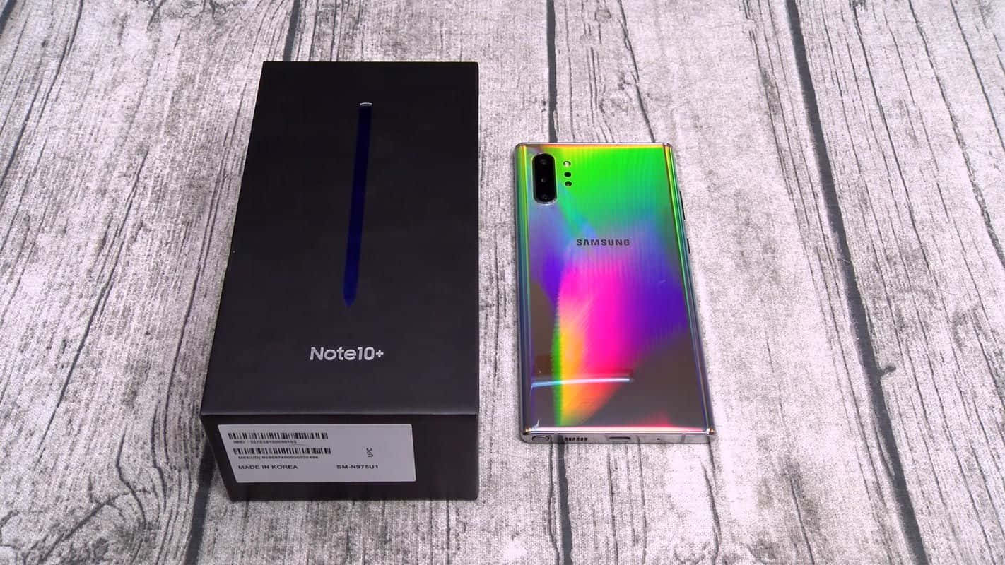 Note 10 桌布 壁紙 — 一部充滿活力的彩虹漸層Samsung Note10+智慧型手機放在其時尚黑色盒子旁邊，置於風化的木質表面上。