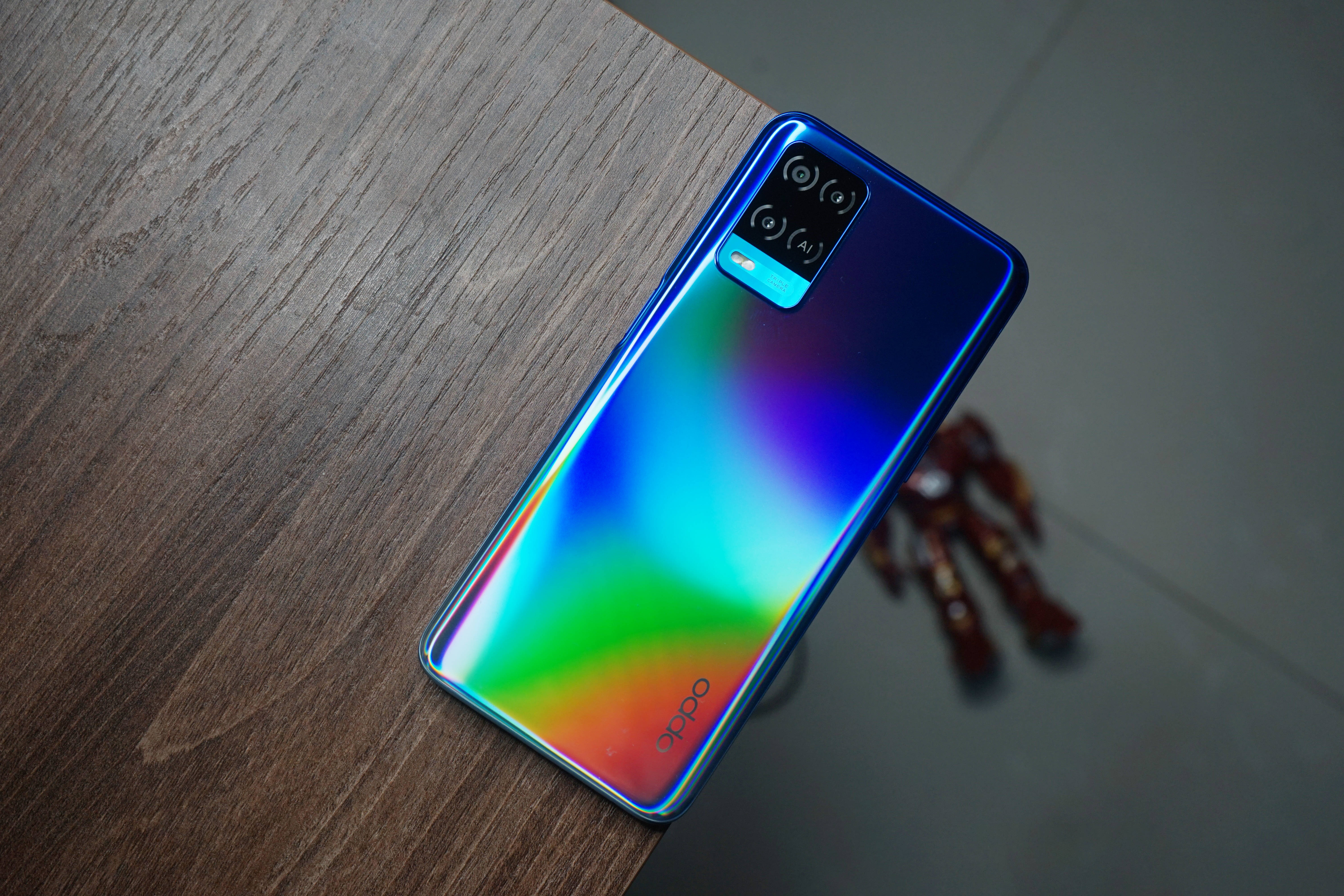 oppo 桌布 壁紙 — 一部充滿活力的彩虹漸層智慧型手機斜放在深色木桌上，背景有一個模糊的金屬物體。