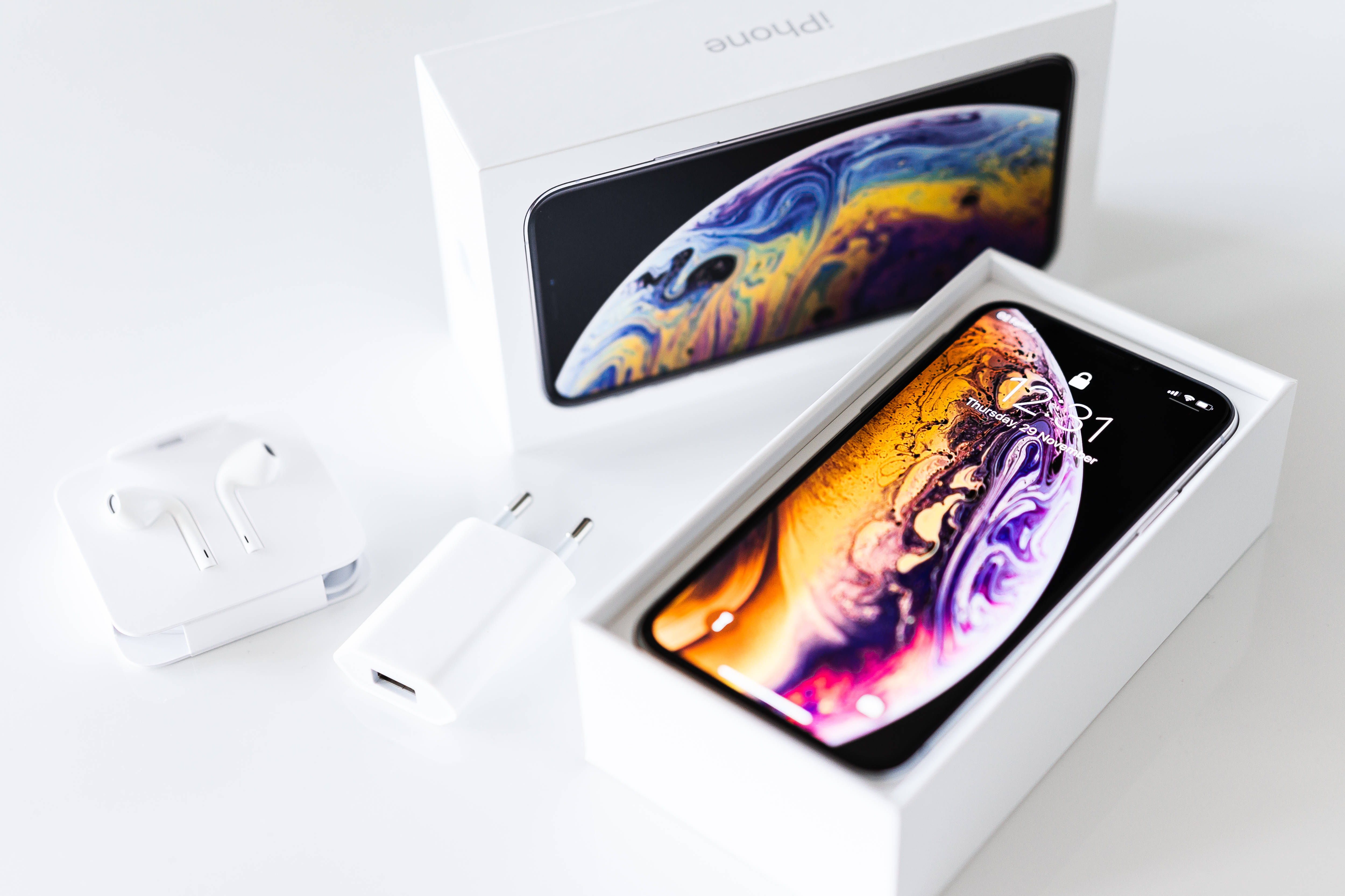 Screen 桌布 壁紙 — 一部全新的iPhone XS打開放在盒中，耳機和充電器放在旁邊的潔白表面上。