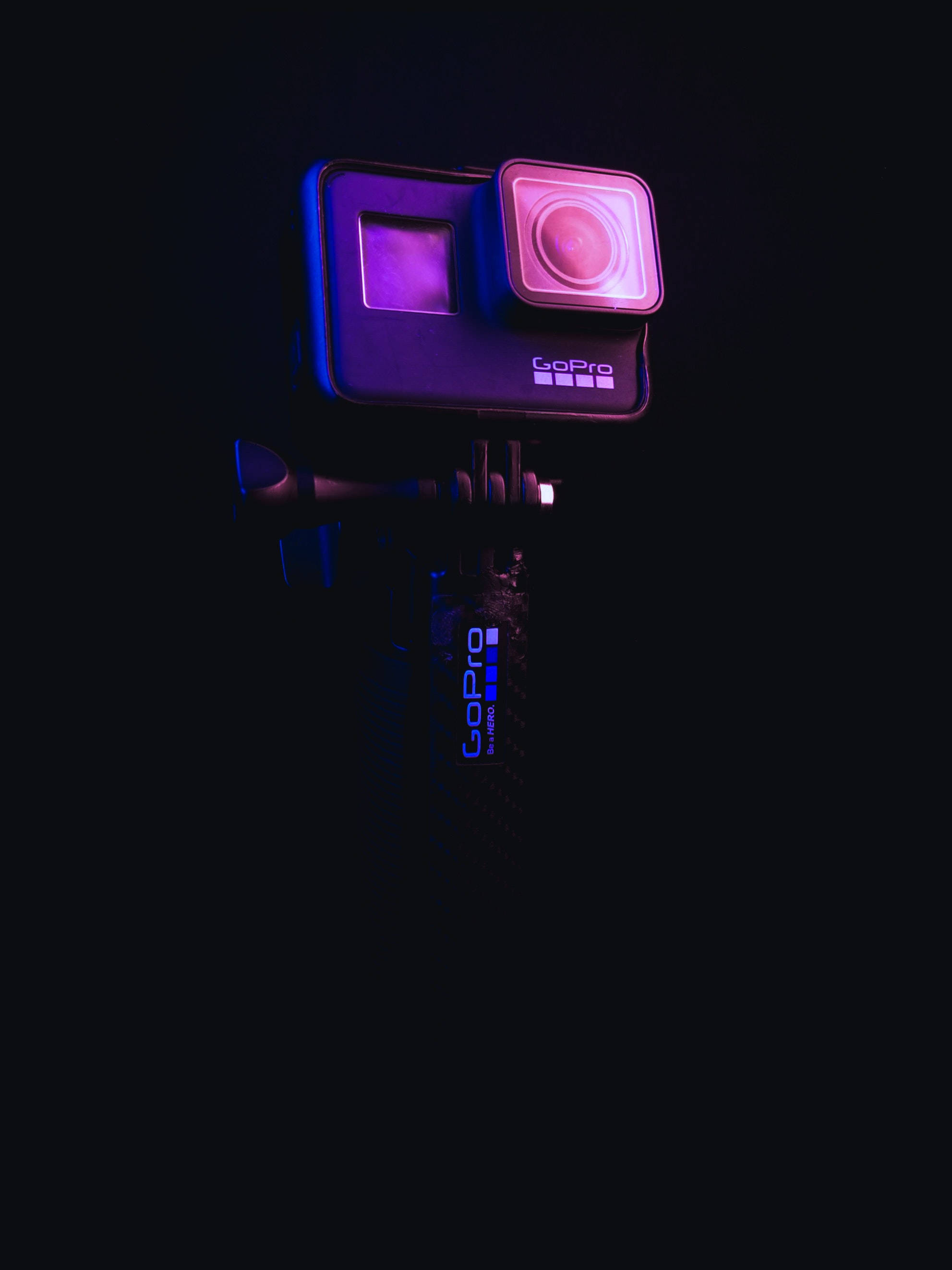 攝影 桌布 壁紙 — 一部安裝在黑色三腳架臂上的GoPro相機，在漆黑背景下散發出鮮豔的紫色和藍色霓虹燈光。